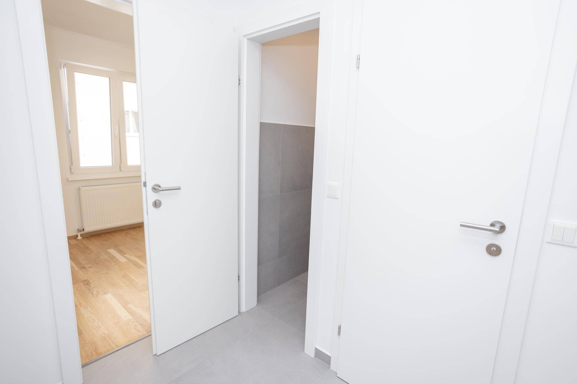 Flur mit Zugang zu einem Zimmer mit Parkettboden und einem gefliesten Abstellraum oder Hauswirtschaftsraum.