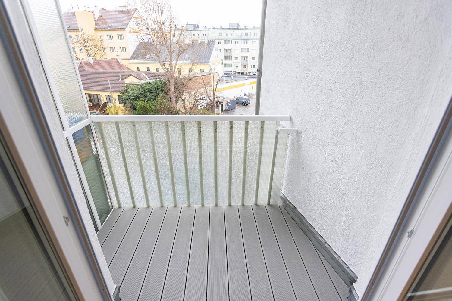 Balkon mit Holzdielen und Blick auf die umliegende Wohngegend und grüne Bäume.