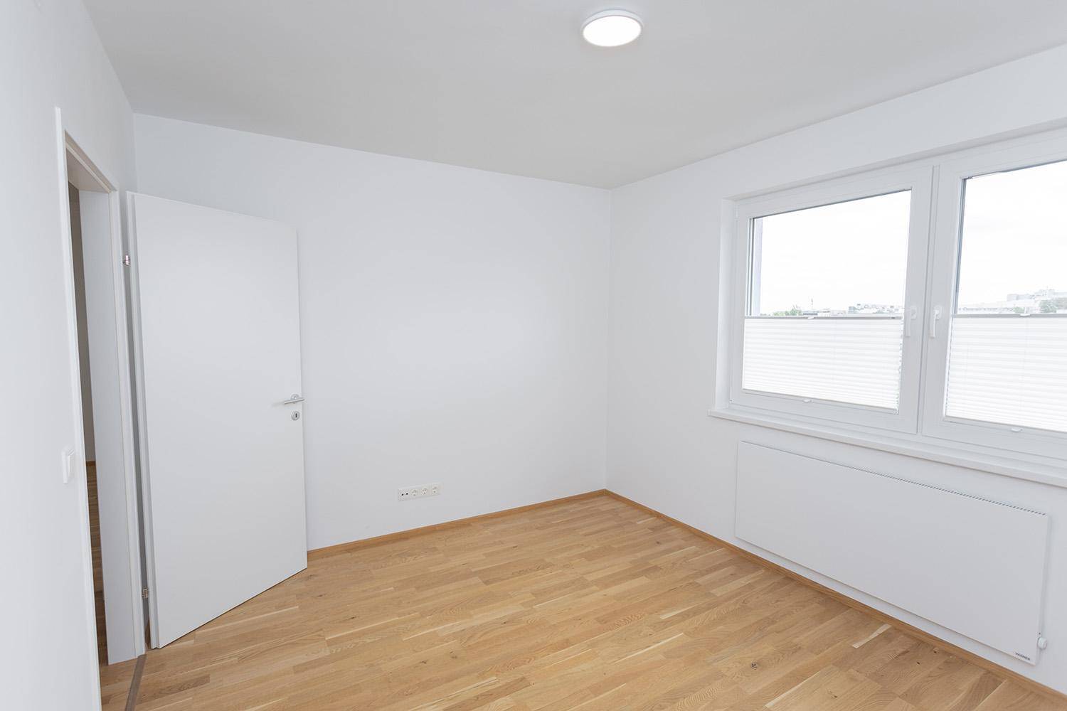 Leeres Schlafzimmer mit Eichenparkett und weiß gestrichenen Wänden, schlicht und hell.