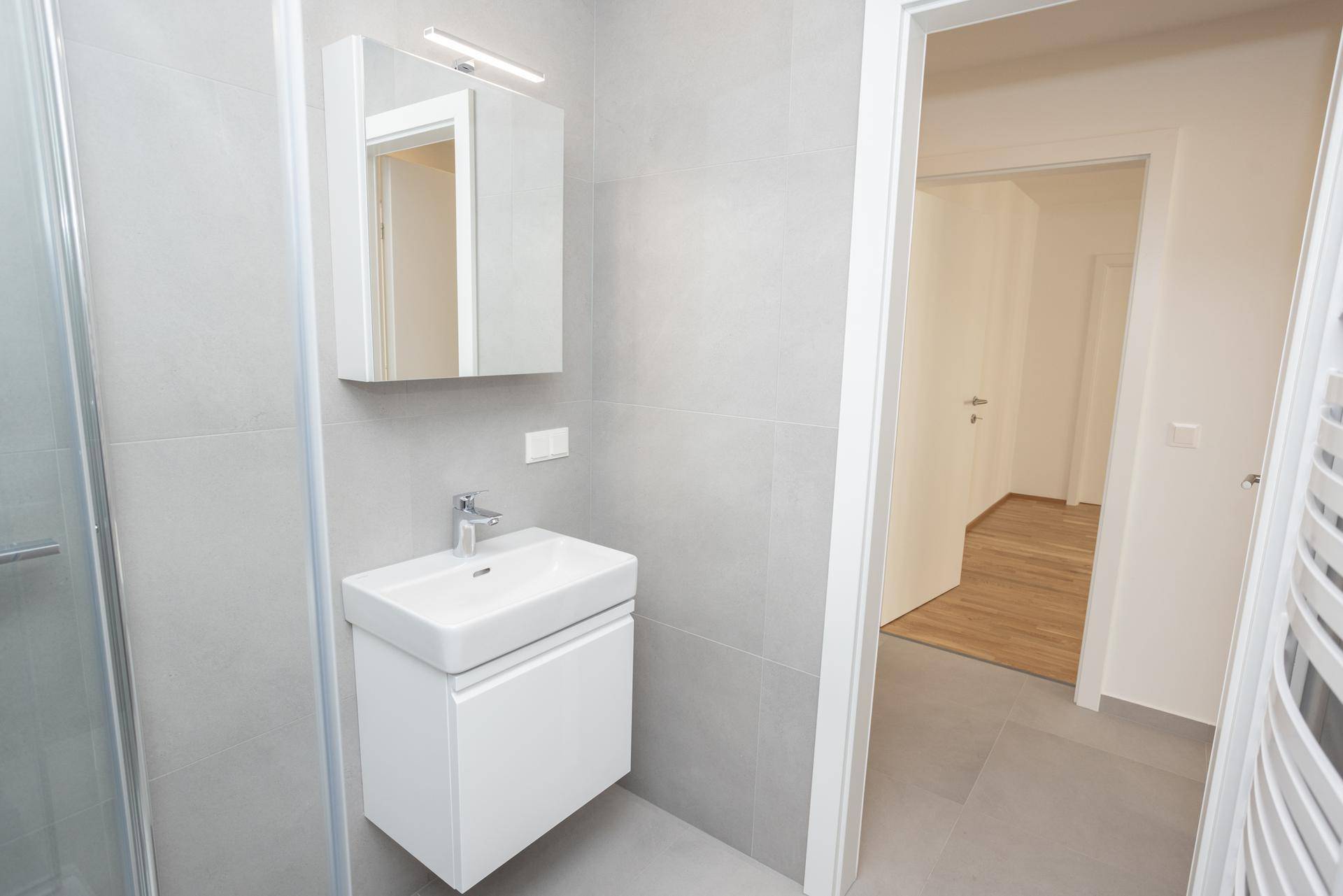 Badezimmer mit modernem Waschbecken, Spiegelschrank und Blick in den angrenzenden Flur.