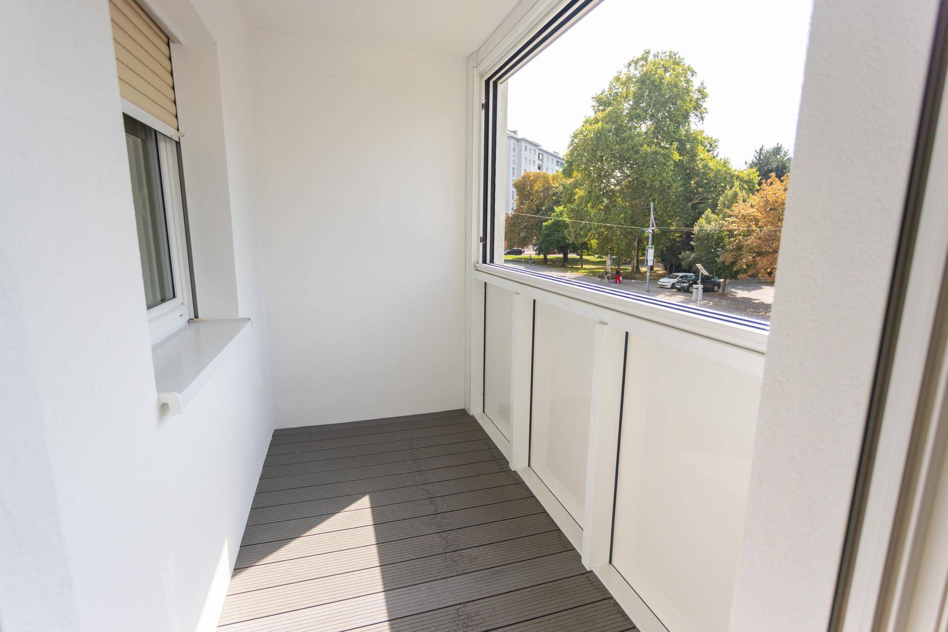 Heller Balkon mit Holzdielenboden und weitem Blick auf die Stadt und grüne Bäume.