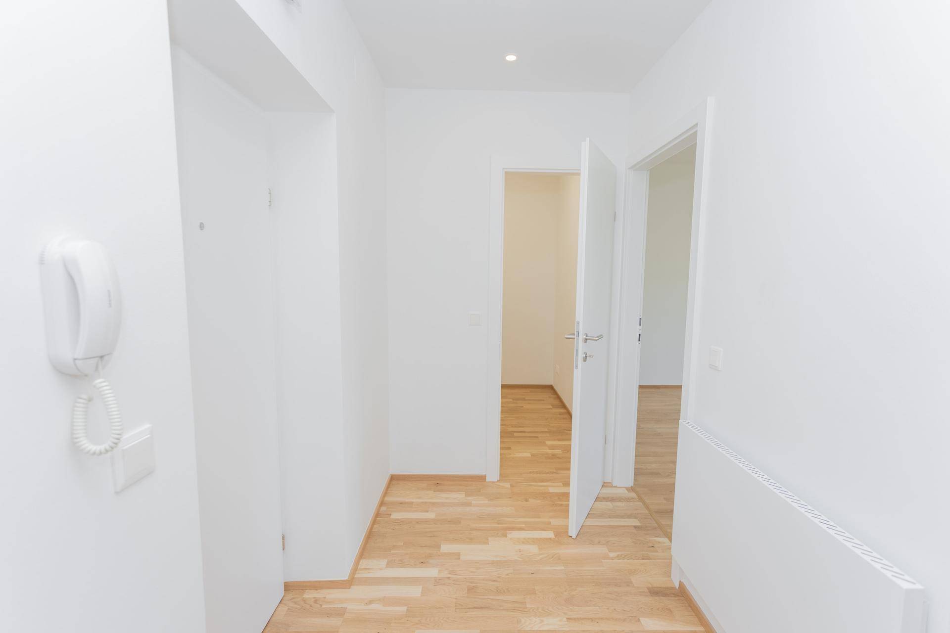 Leerer, heller Flur mit Parkettboden und weißen Wänden, bereit zur individuellen Gestaltung der Wohnung.