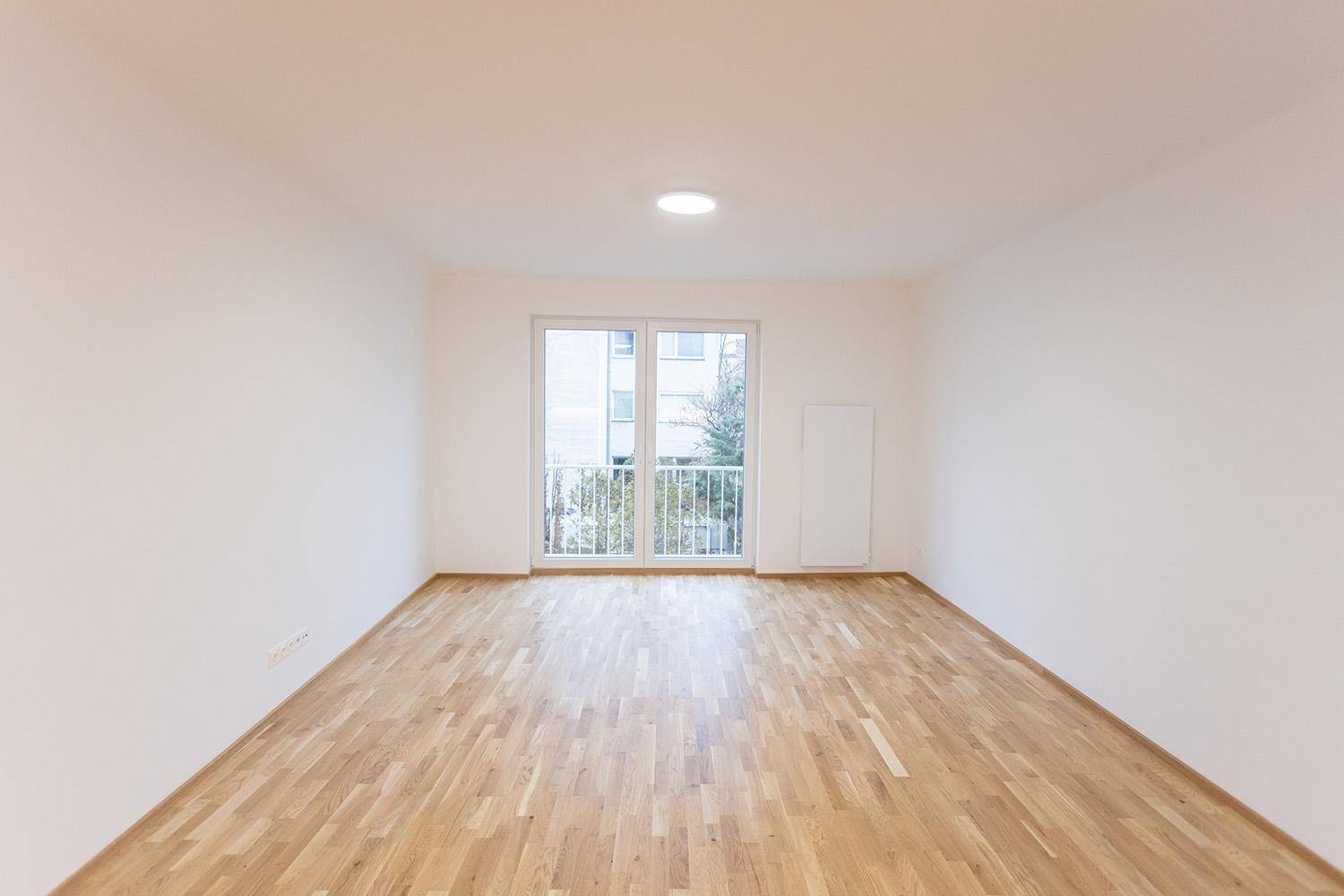 Helles, leeres Zimmer mit Holzboden und Zugang zu einem Balkon, ideal als Wohnbereich.