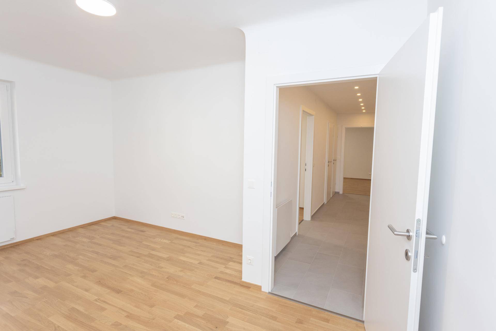 Helles Zimmer mit Holzparkettboden und offener Tür zum Flur, bereit zur Einrichtung.