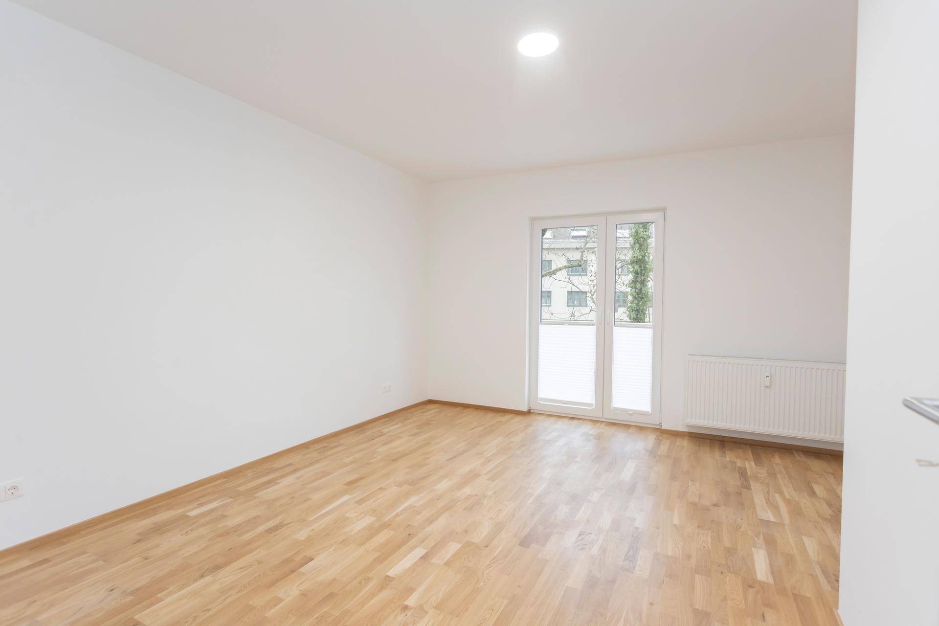 Helles Schlafzimmer mit Parkettboden und Zugang zu einem französischen Balkon.