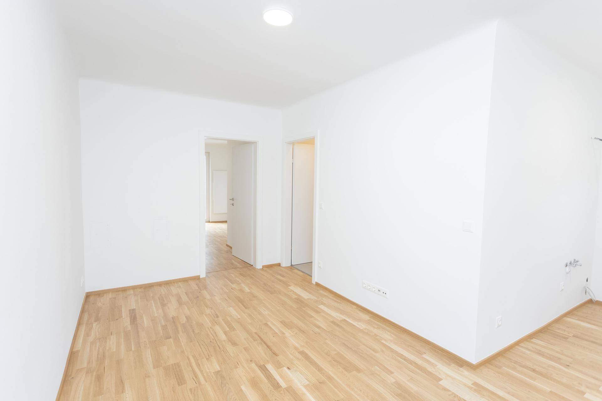 Heller, leerer Raum mit Holzfußboden und Zugang zu zwei weiteren Zimmern.