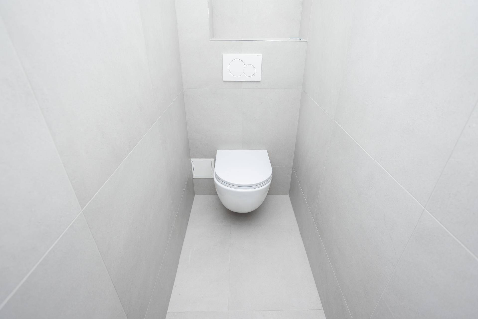 Separates WC mit wandhängender Toilette und modernen grauen Fliesen an Wänden und Boden.