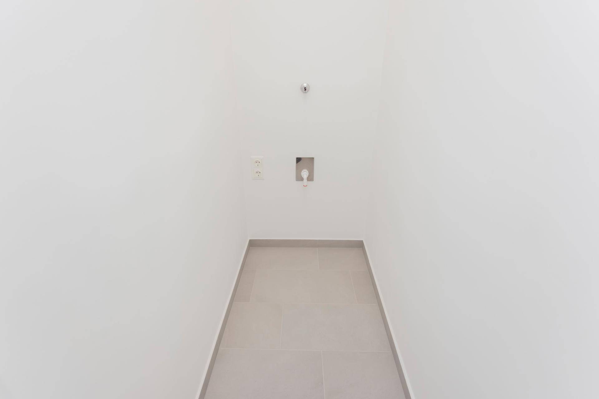 Kleiner Hauswirtschaftsraum mit Fliesenboden und Anschlüssen für Waschmaschine und Trockner.