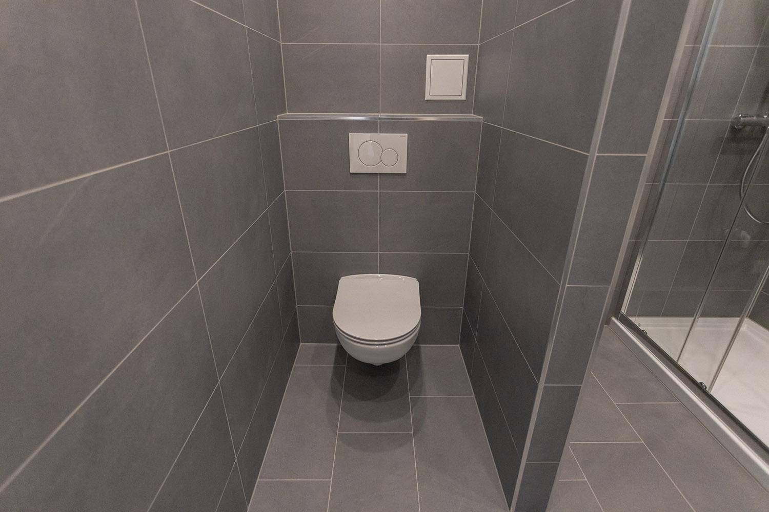 Wandhängendes WC in einem modern gefliesten Badezimmer mit schlichtem Design und grauen Fliesen.