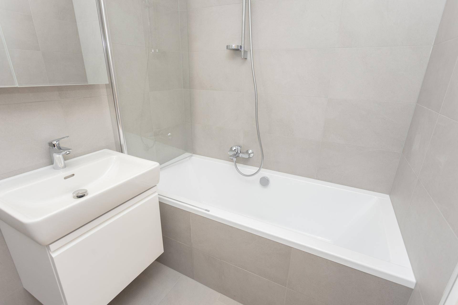 Modernes Badezimmer mit Badewanne, Duschabtrennung und Waschbecken mit Unterschrank, hell gefliest.