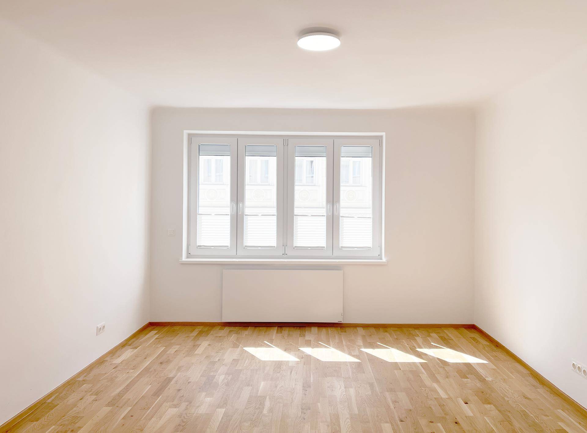 Helles, leeres Zimmer mit Parkettboden und Fensterfront.
