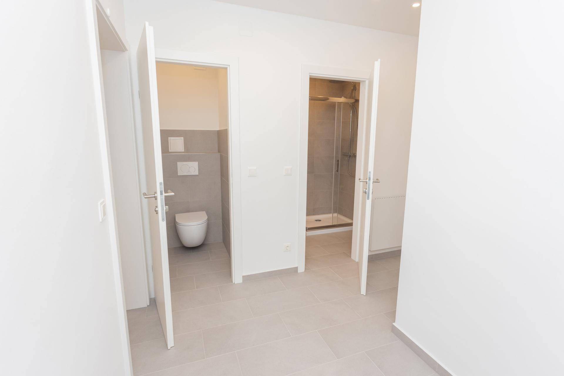 Flurbereich mit Zugang zu separatem WC und modernem Duschbad, beide mit Fliesenboden.