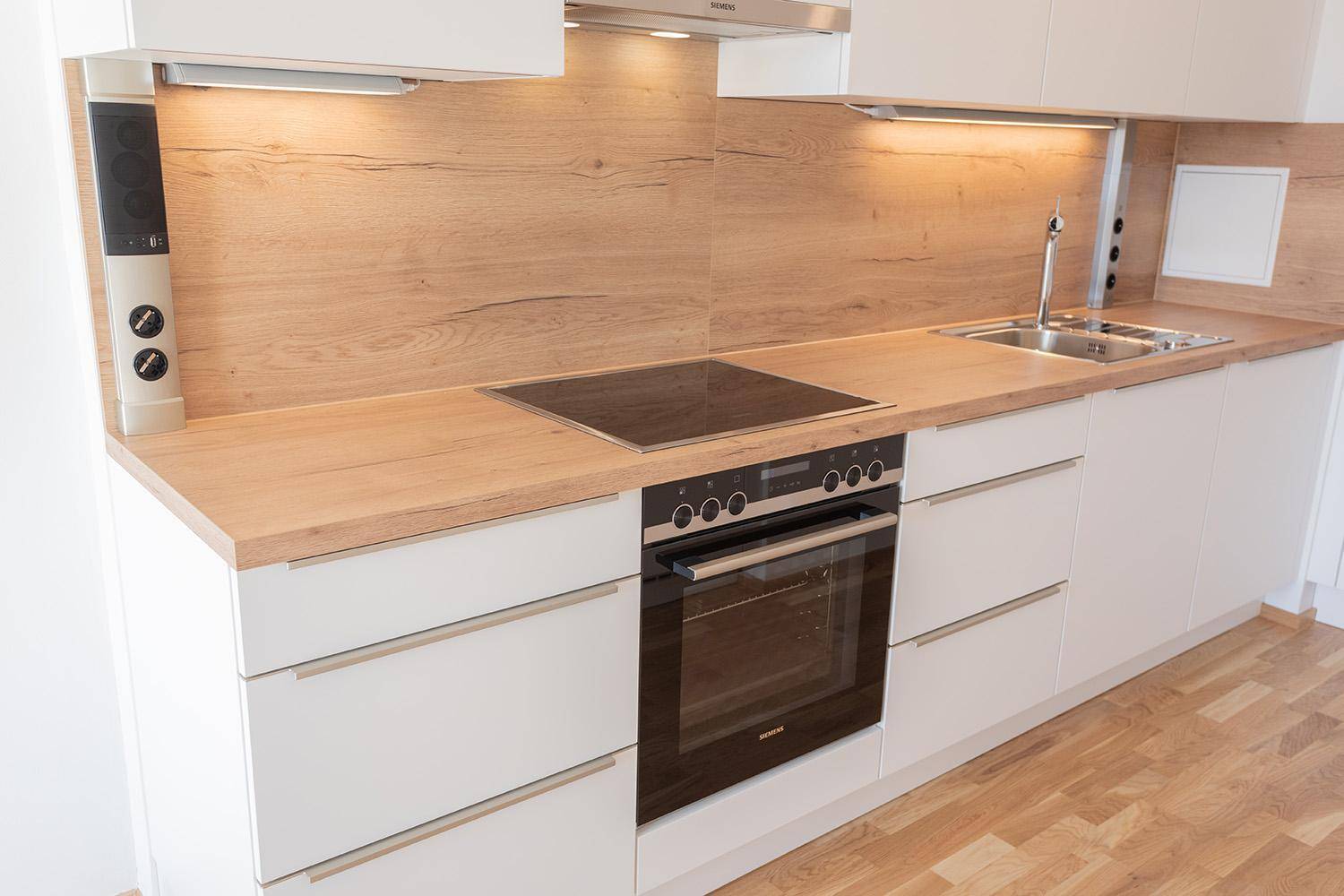 Detailansicht der modernen Küche mit Induktionskochfeld, Backofen und Spüle.