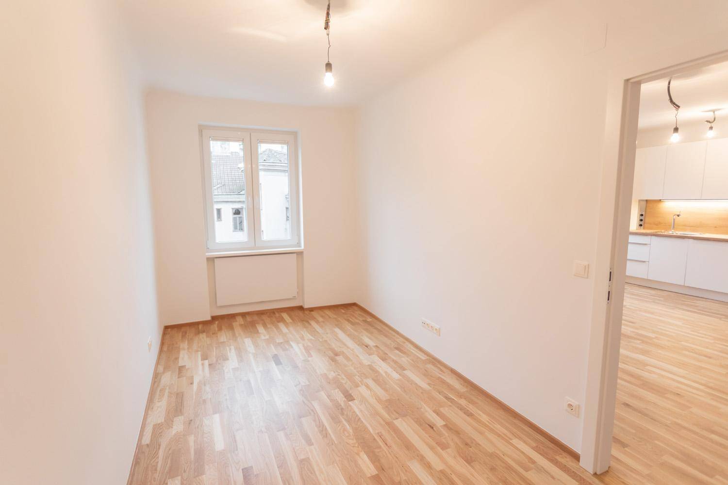 Helles Zimmer mit Parkettboden und Blick auf den Küchenbereich.
