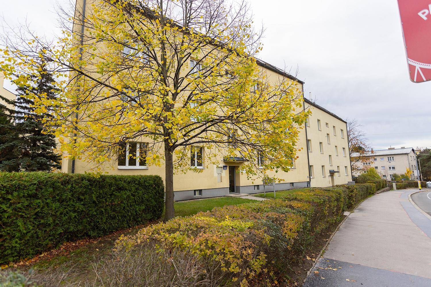 Mehrfamilienhaus mit gelber Fassade, umgeben von Bäumen und Hecken.