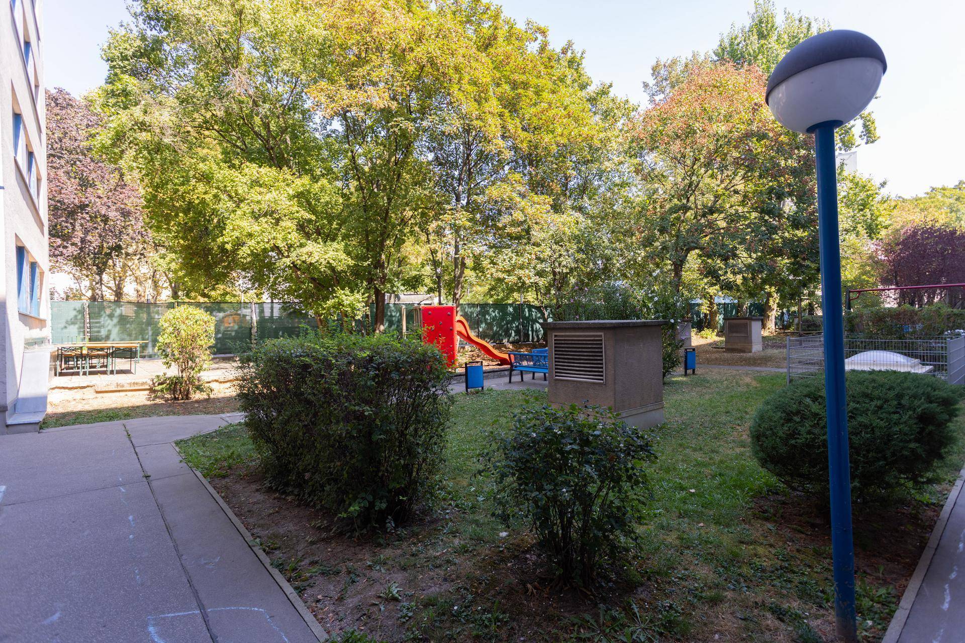 Grüner Gemeinschaftsgarten mit Spielplatz und Sitzgelegenheiten unter Bäumen.