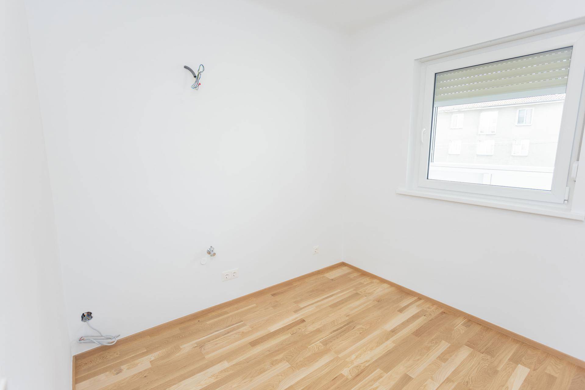 Leerer Raum mit Holzboden und Fenster, vorbereitet für die Installation einer Küche.