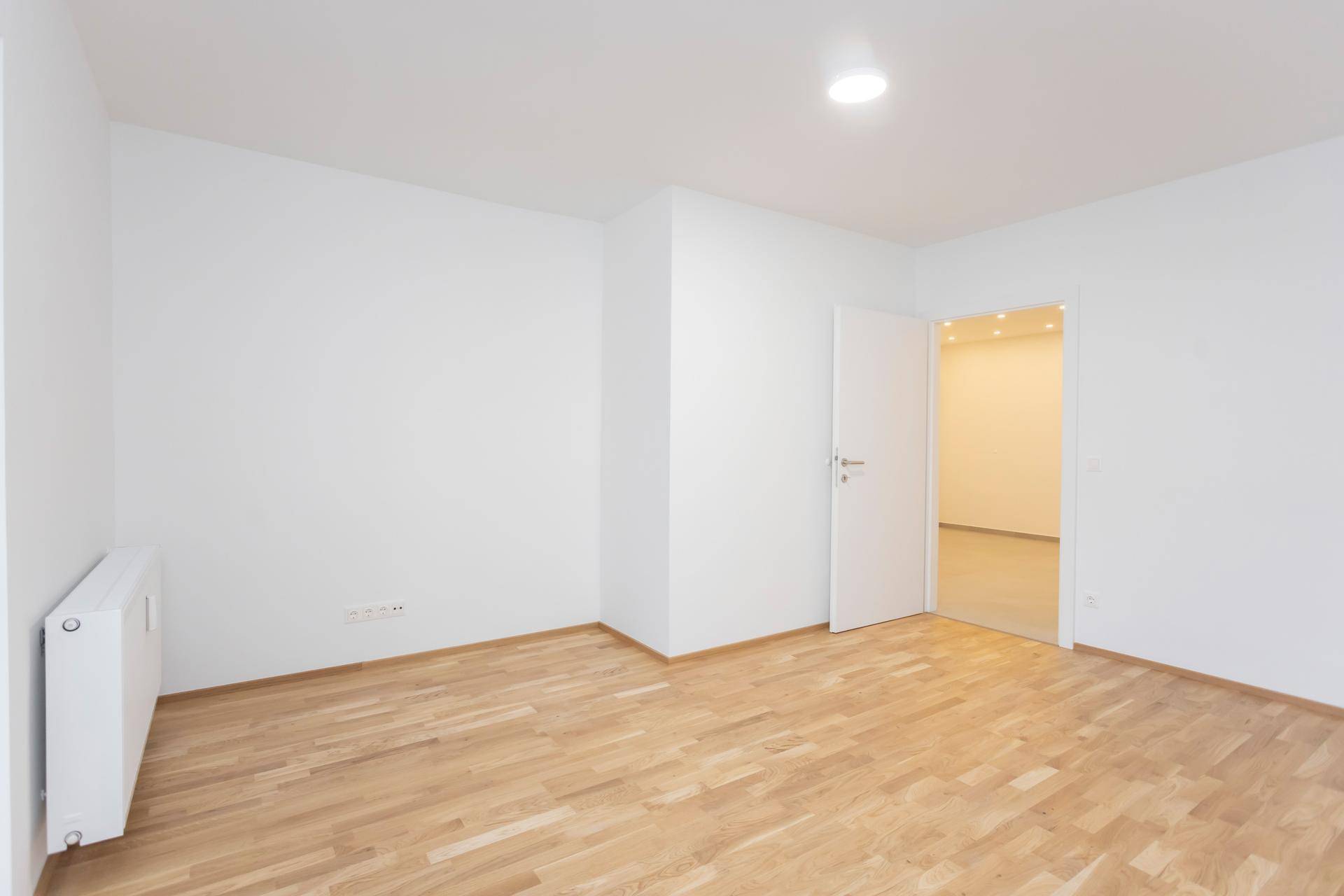 Helles, leeres Zimmer mit Parkettboden und weißen Wänden, bereit zur individuellen Gestaltung.