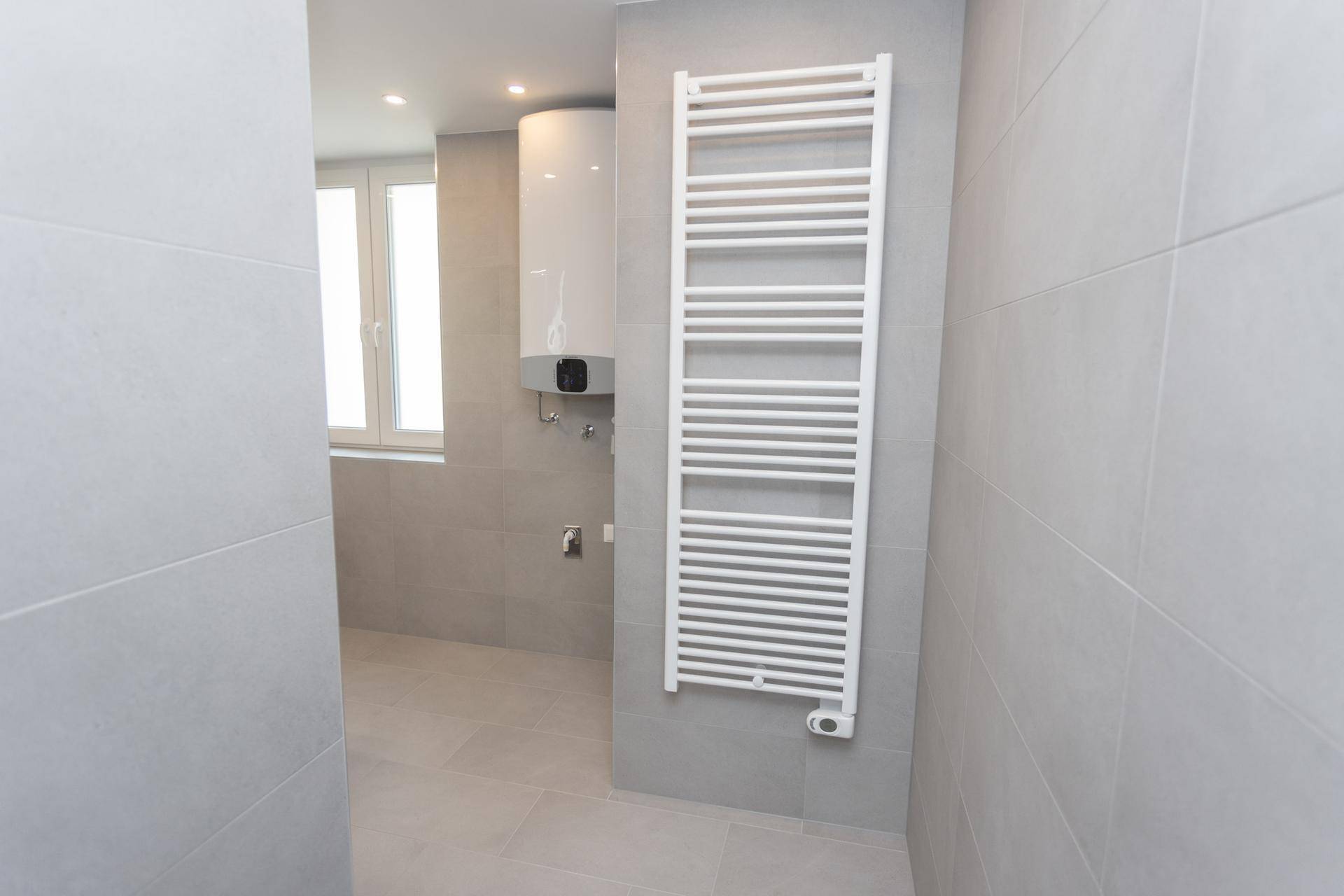 Badezimmer mit modernen grauen Fliesen und einem praktischen Handtuchheizkörper.