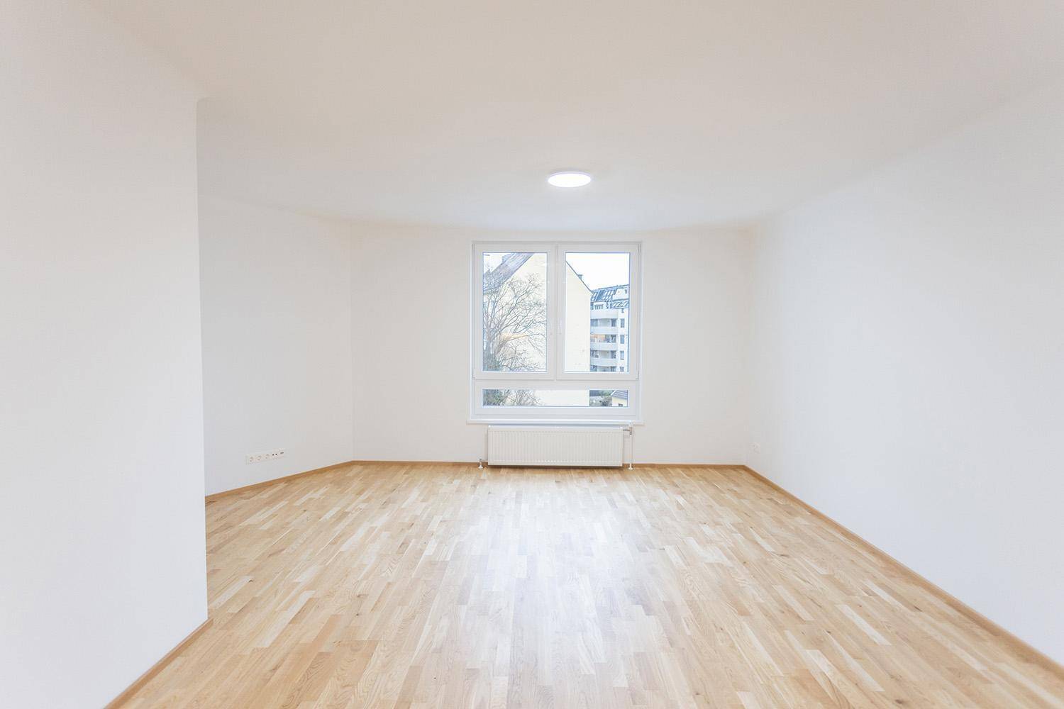 Geräumiges Wohnzimmer mit Holzboden und großem Fenster, das viel Tageslicht hereinlässt.