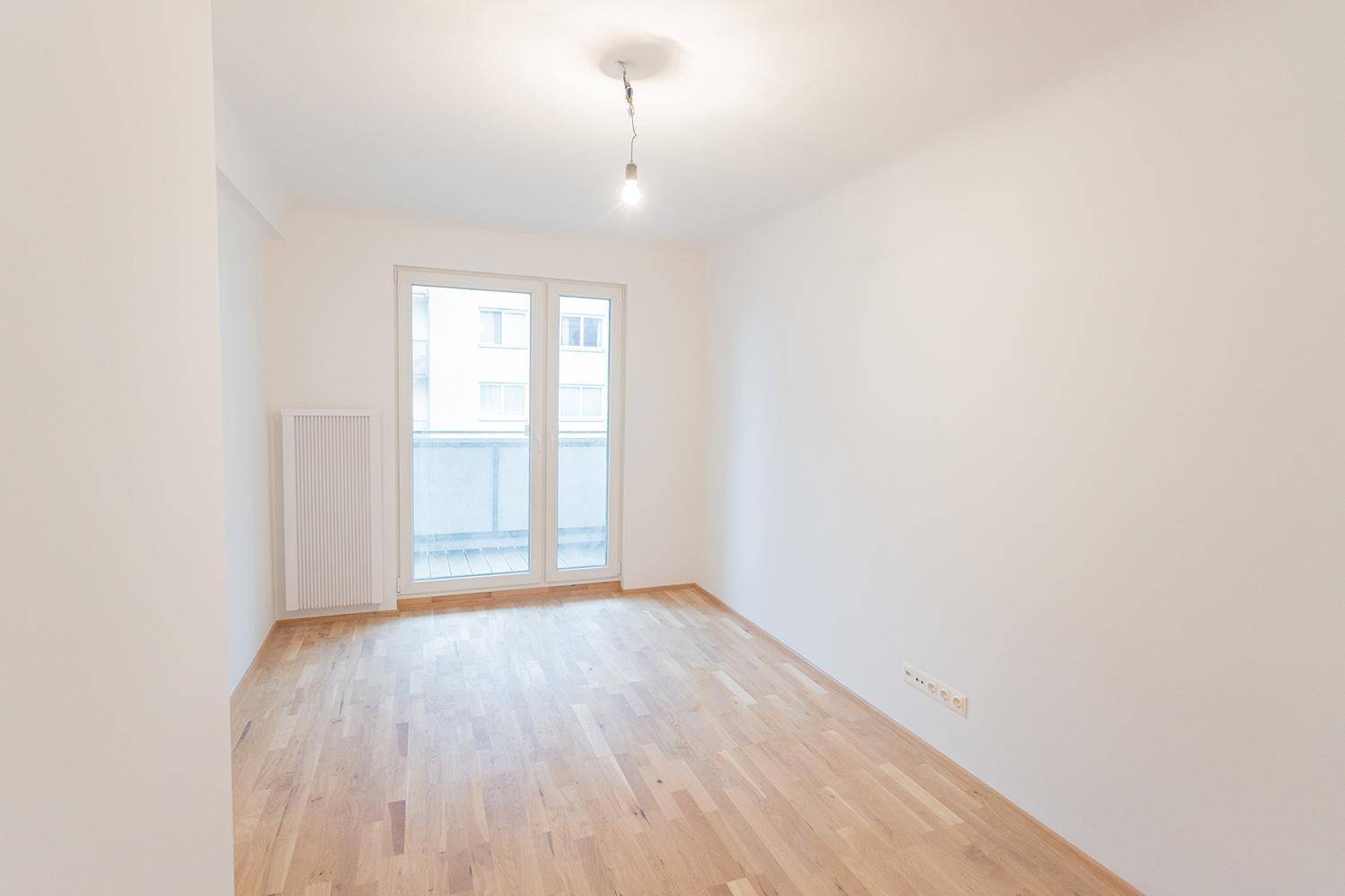 Helles, leeres Zimmer mit Parkettboden und Zugang zu einem Balkon durch Doppeltüren.