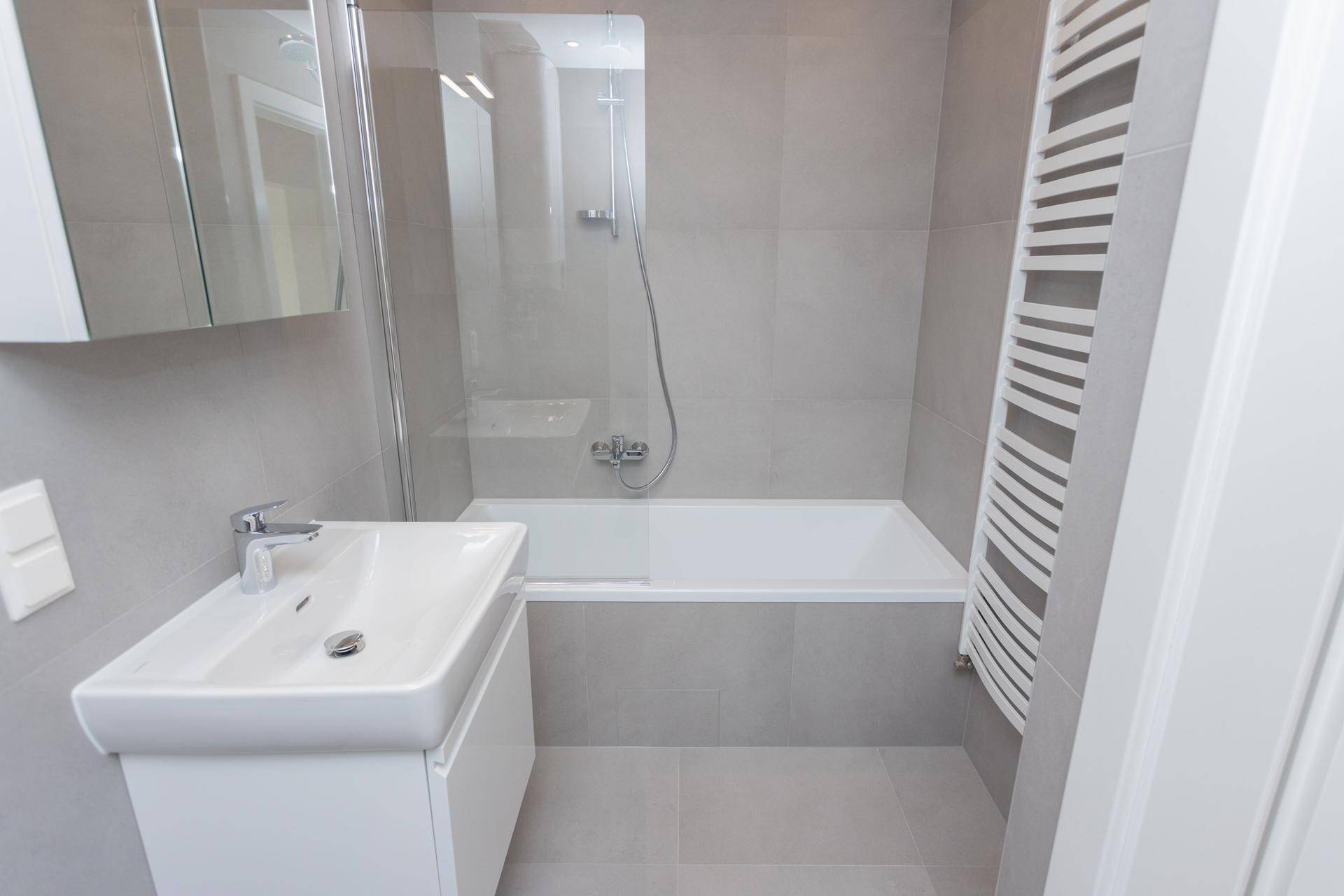 Helles Badezimmer mit Badewanne, Duschabtrennung, Waschbecken und beheiztem Handtuchhalter.