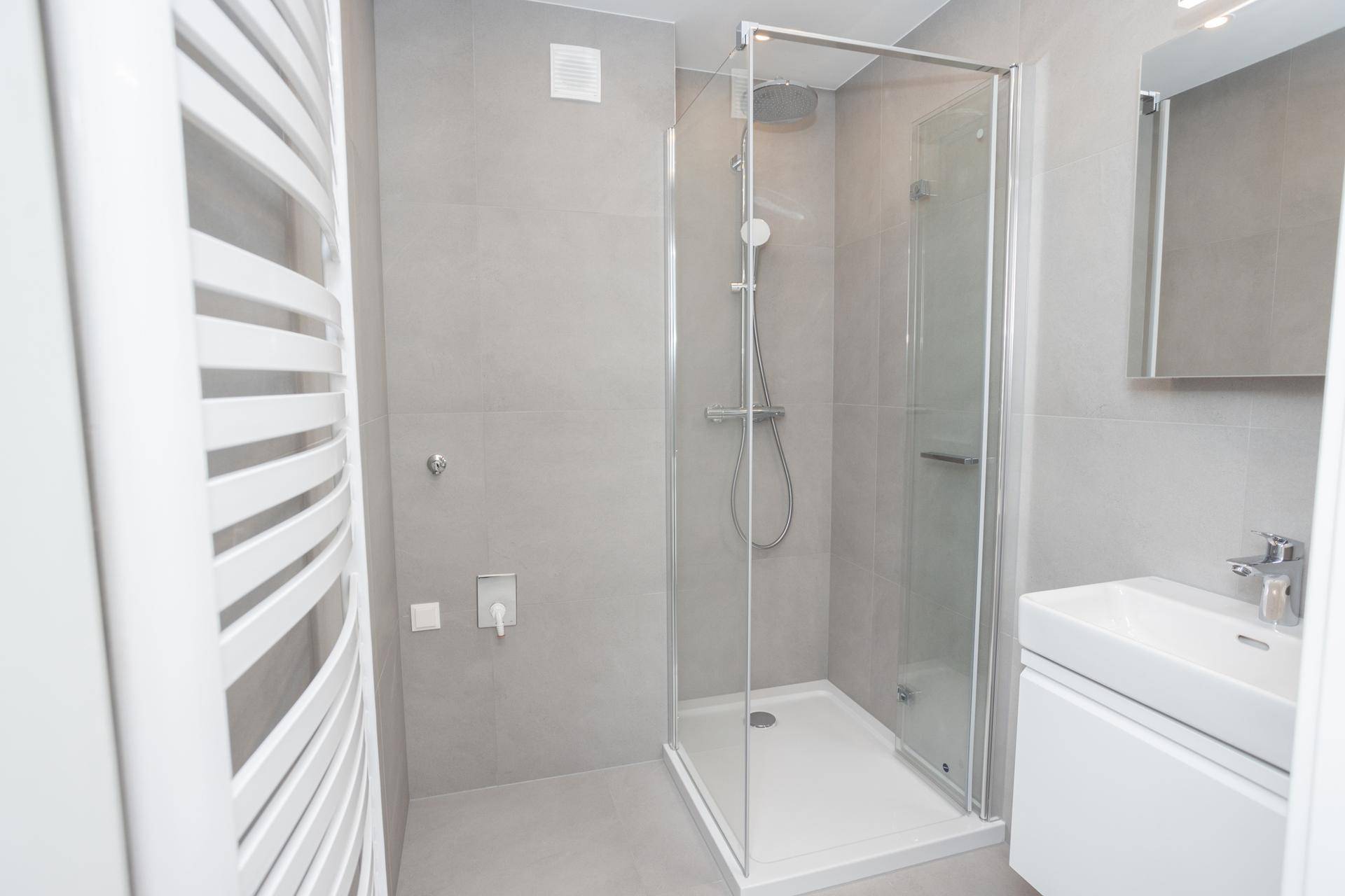 Modernes Badezimmer mit großer Duschkabine, Waschbecken und beheiztem Handtuchhalter.