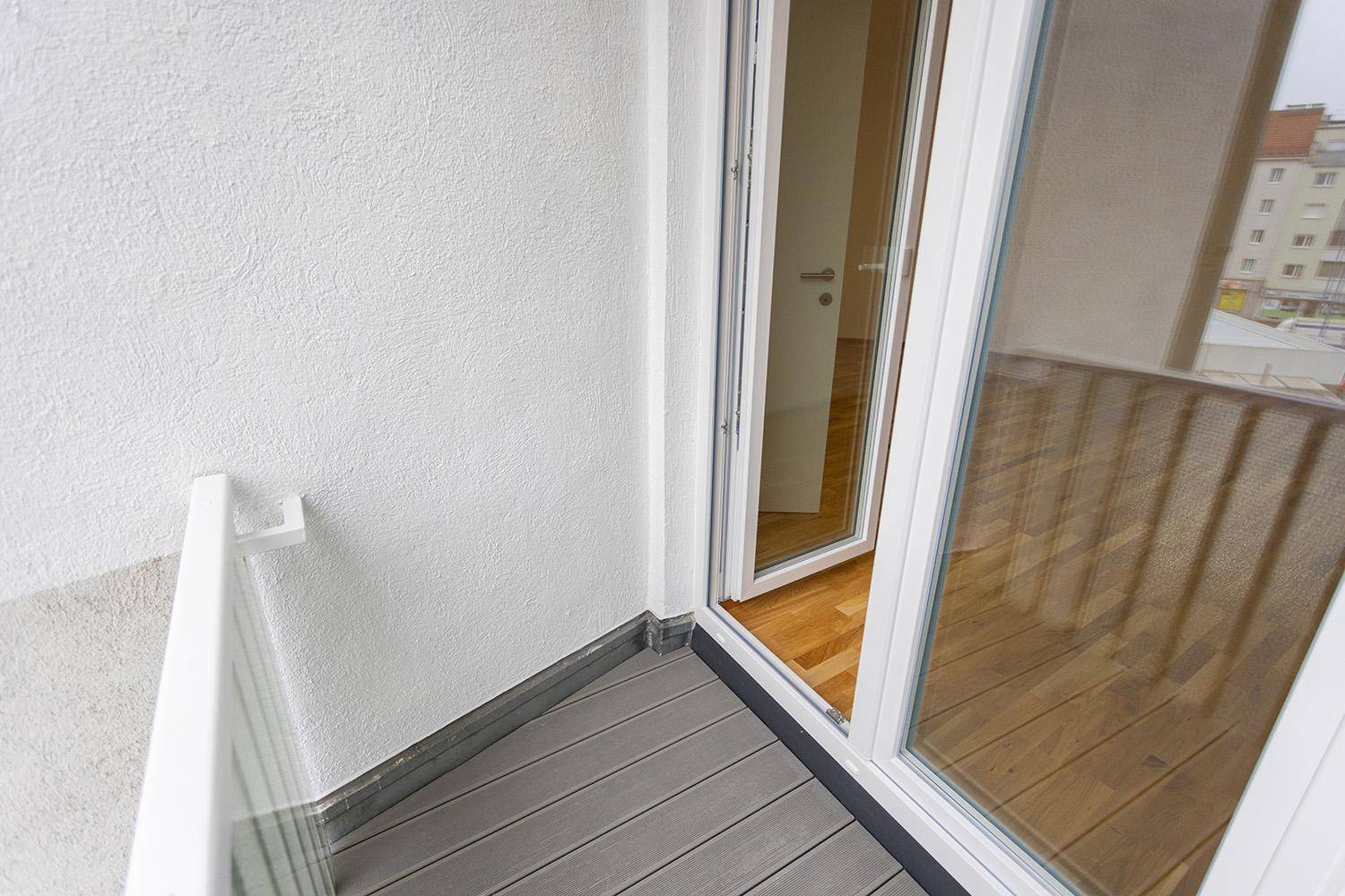 Balkon mit Holzdielen und Blick durch die offene Tür in den hellen Innenraum.