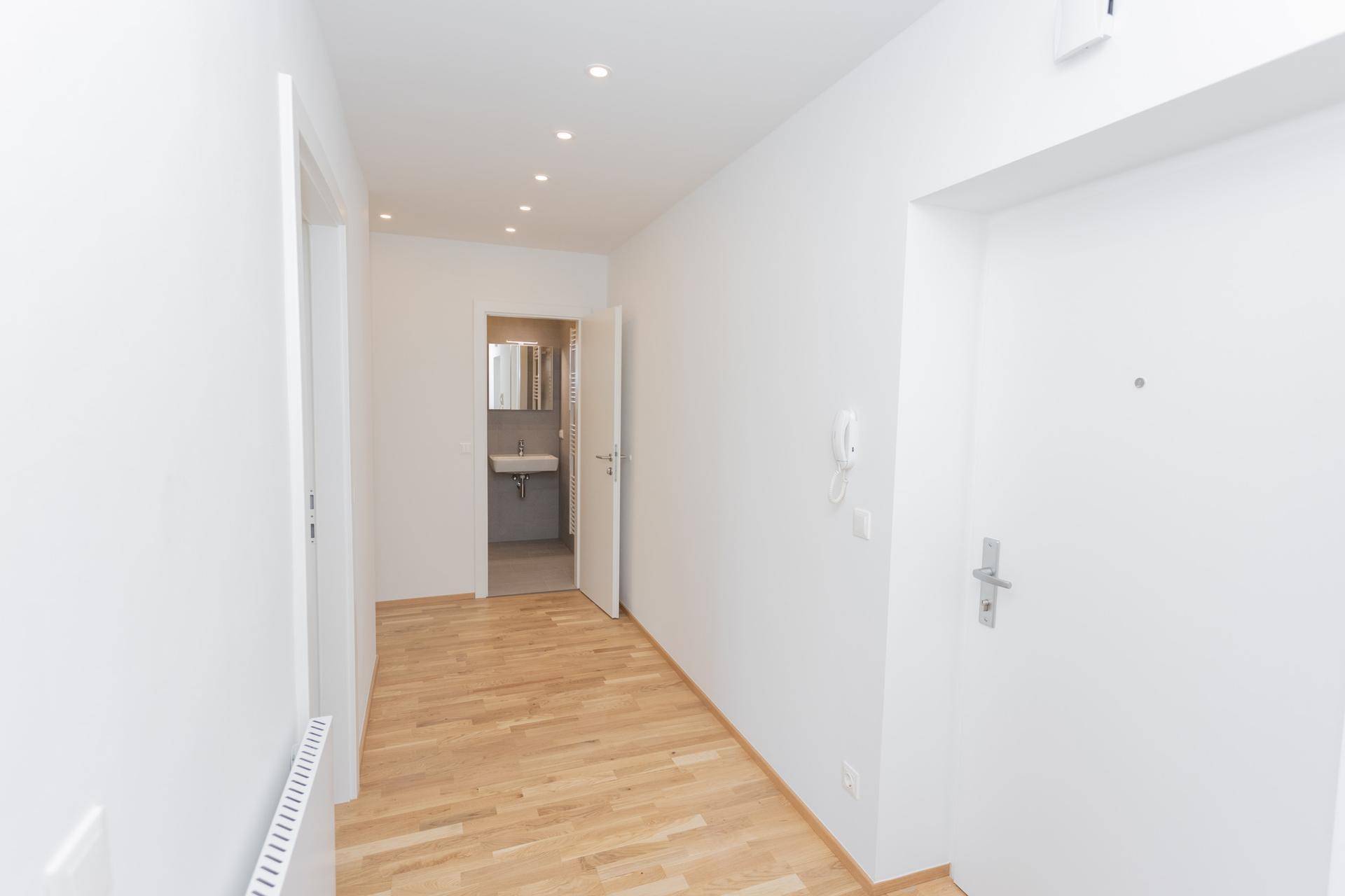 Heller Flur mit Parkettboden und Zugang zu einem modernen Badezimmer, das sich im Hintergrund befindet.