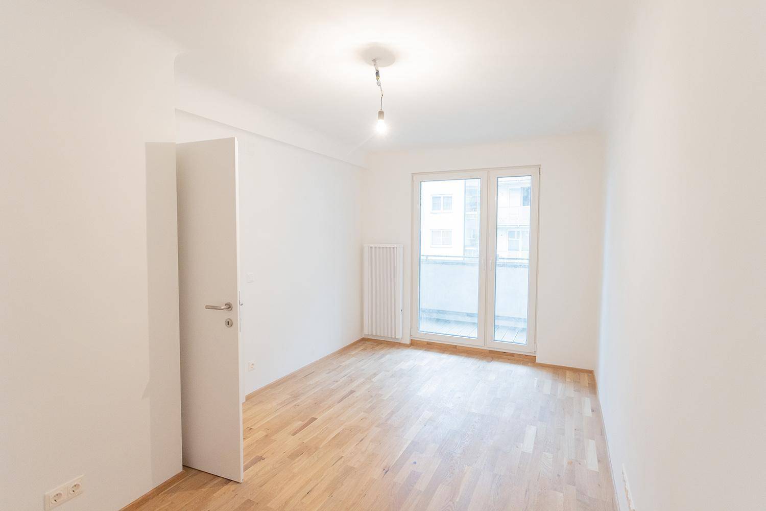 Helles Zimmer mit Parkettboden und Zugang zu einem Balkon, ideal als Wohn- oder Schlafzimmer.