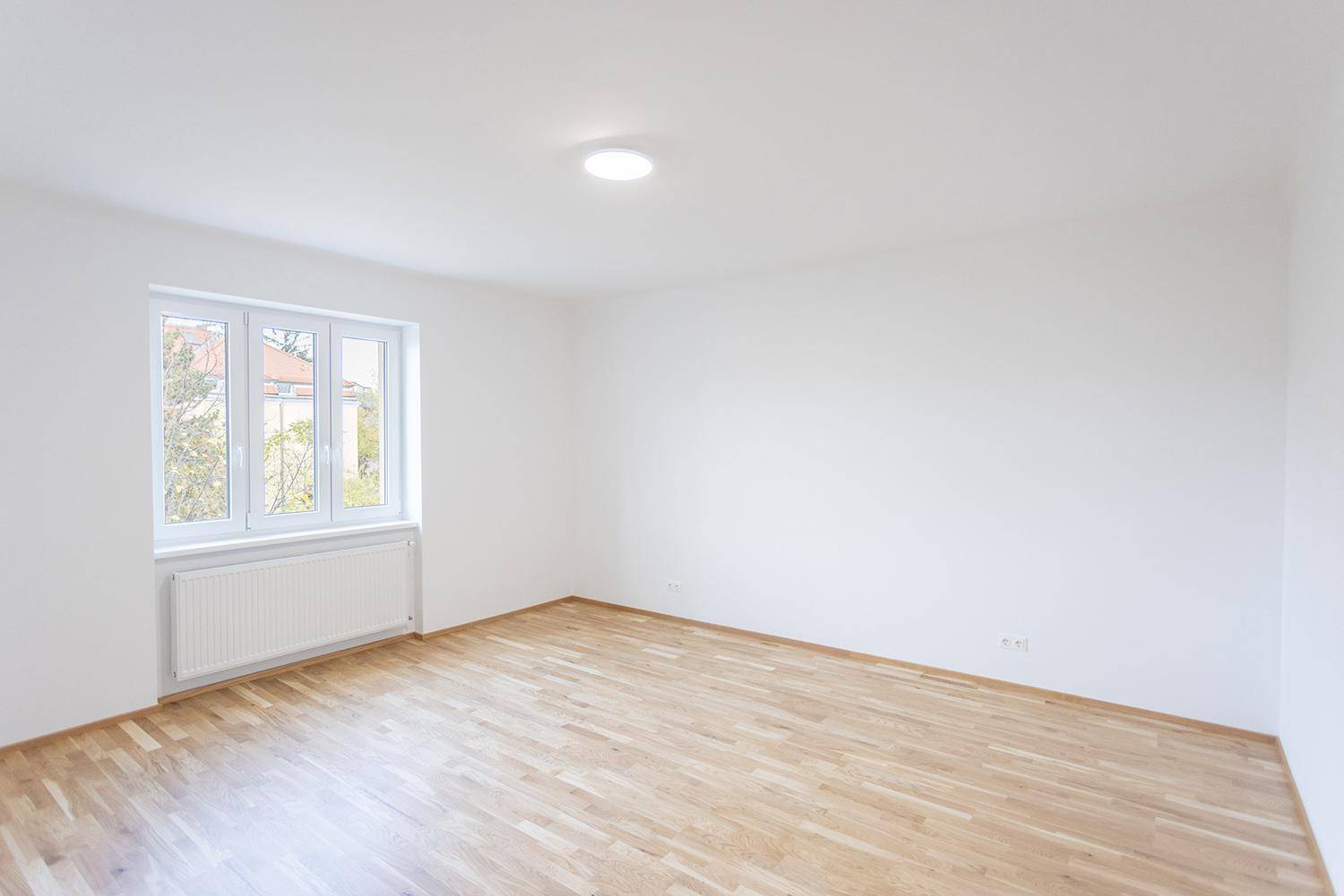 Geräumiges Schlafzimmer mit Holzparkett, weißen Wänden und großem Fenster, unmöbliert.