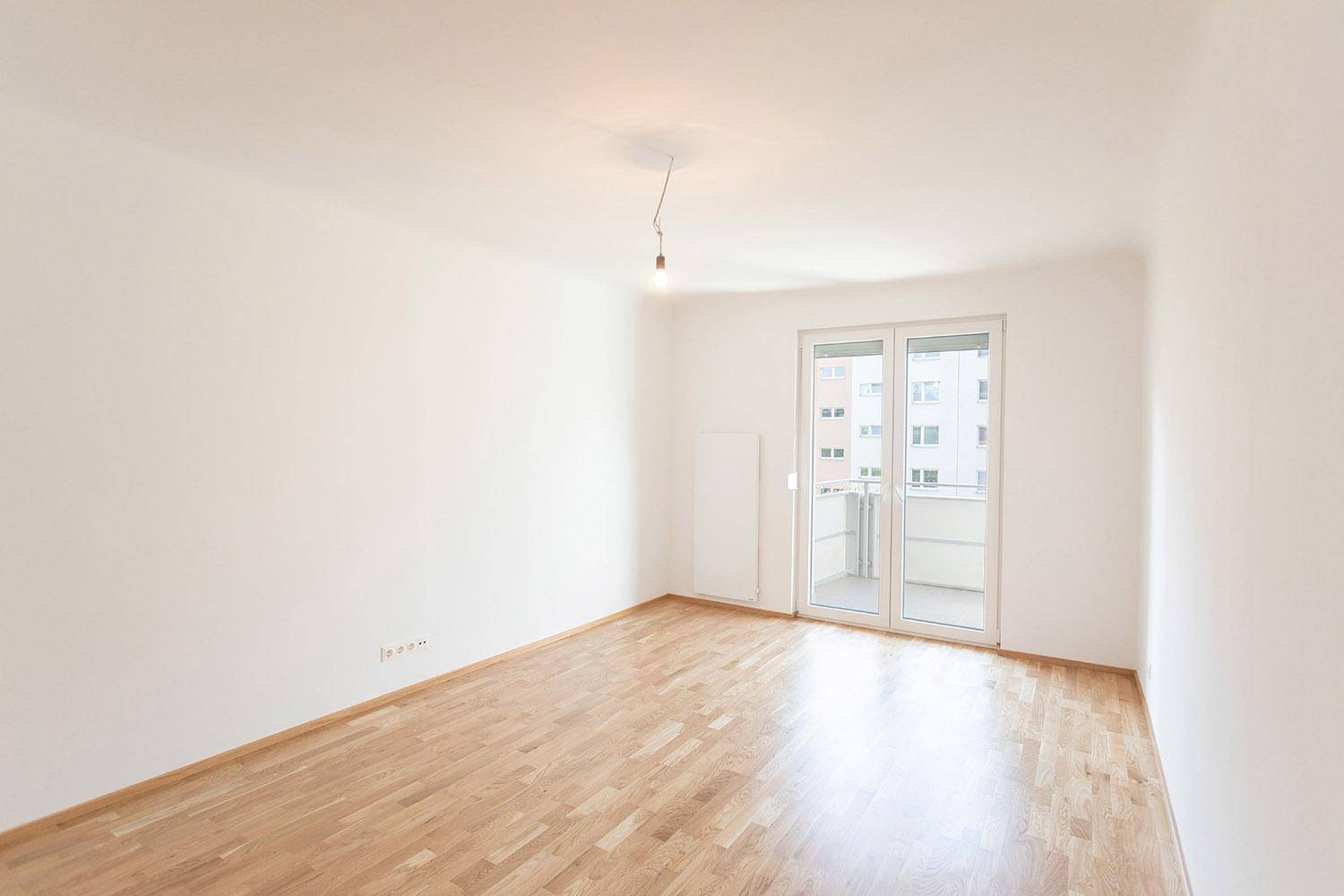 Heller, leerer Raum mit Parkettboden und Balkontür, bereit zur individuellen Gestaltung.