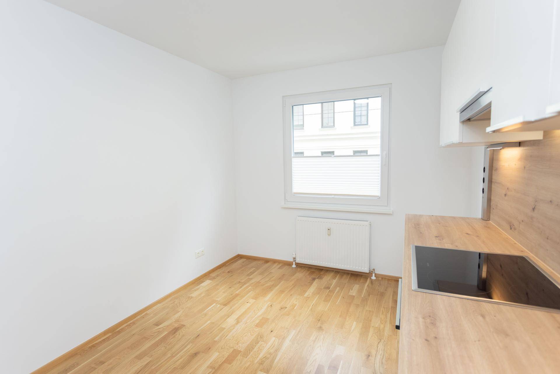 Moderner Küchenbereich mit Holzarbeitsplatte und Induktionskochfeld, daneben ein Fenster.