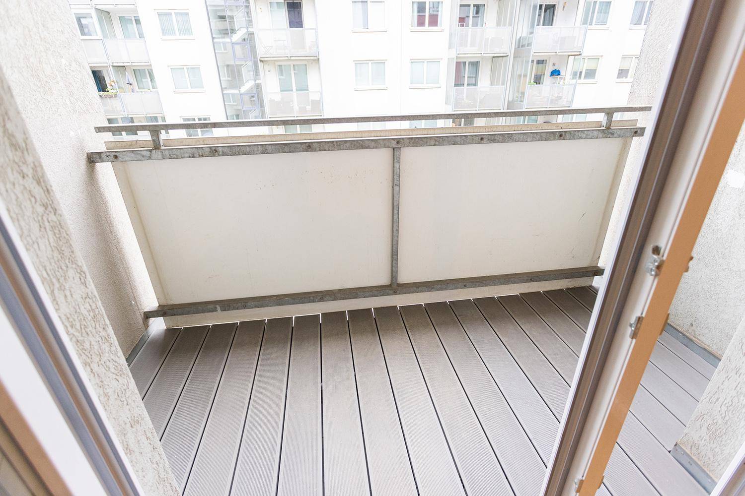 Leerer Balkon mit modernem Holzdeck und Blick auf umliegende Wohngebäude.