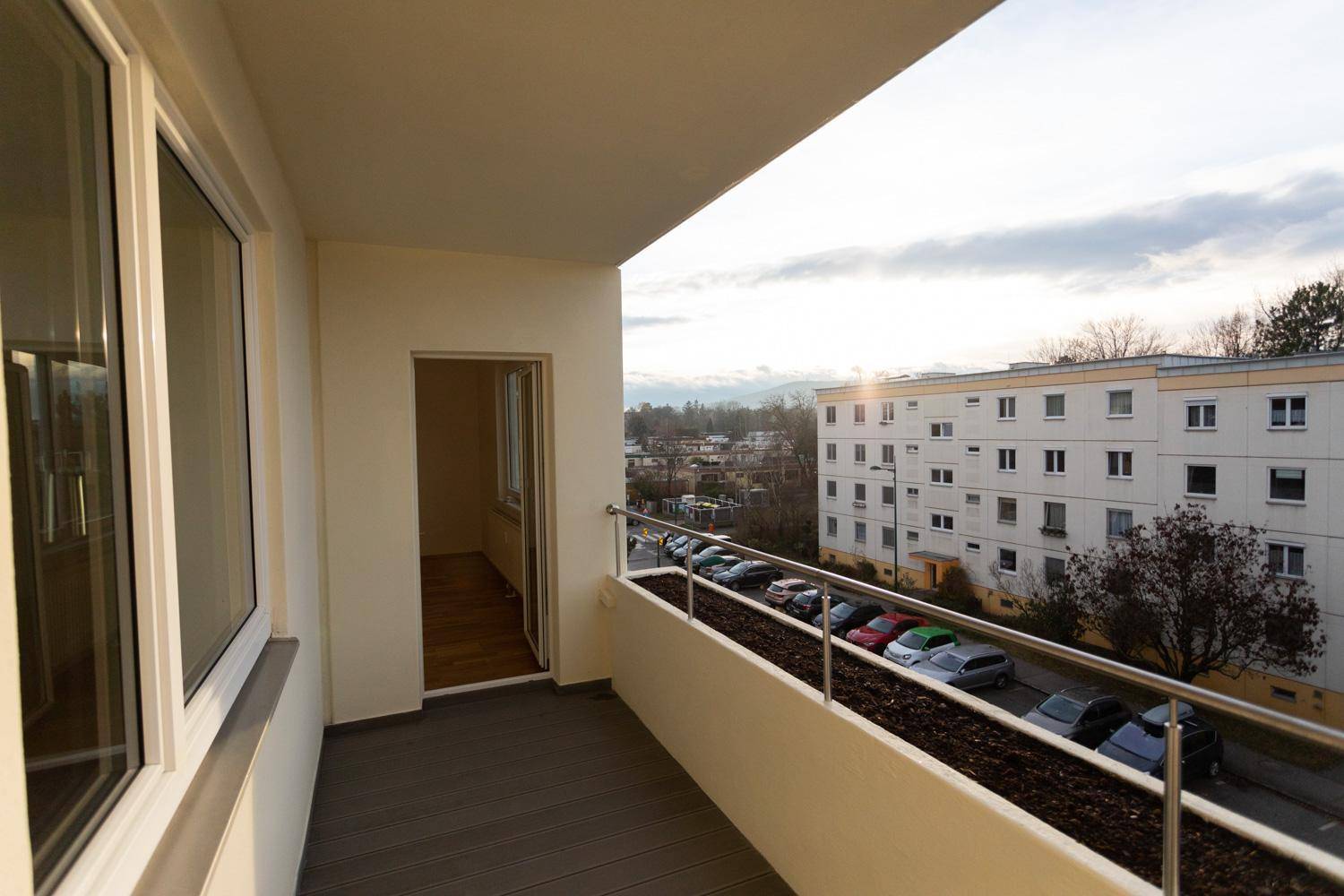 Heller Balkon mit Blick auf die Straße, parkende Autos und Wohngebäude.