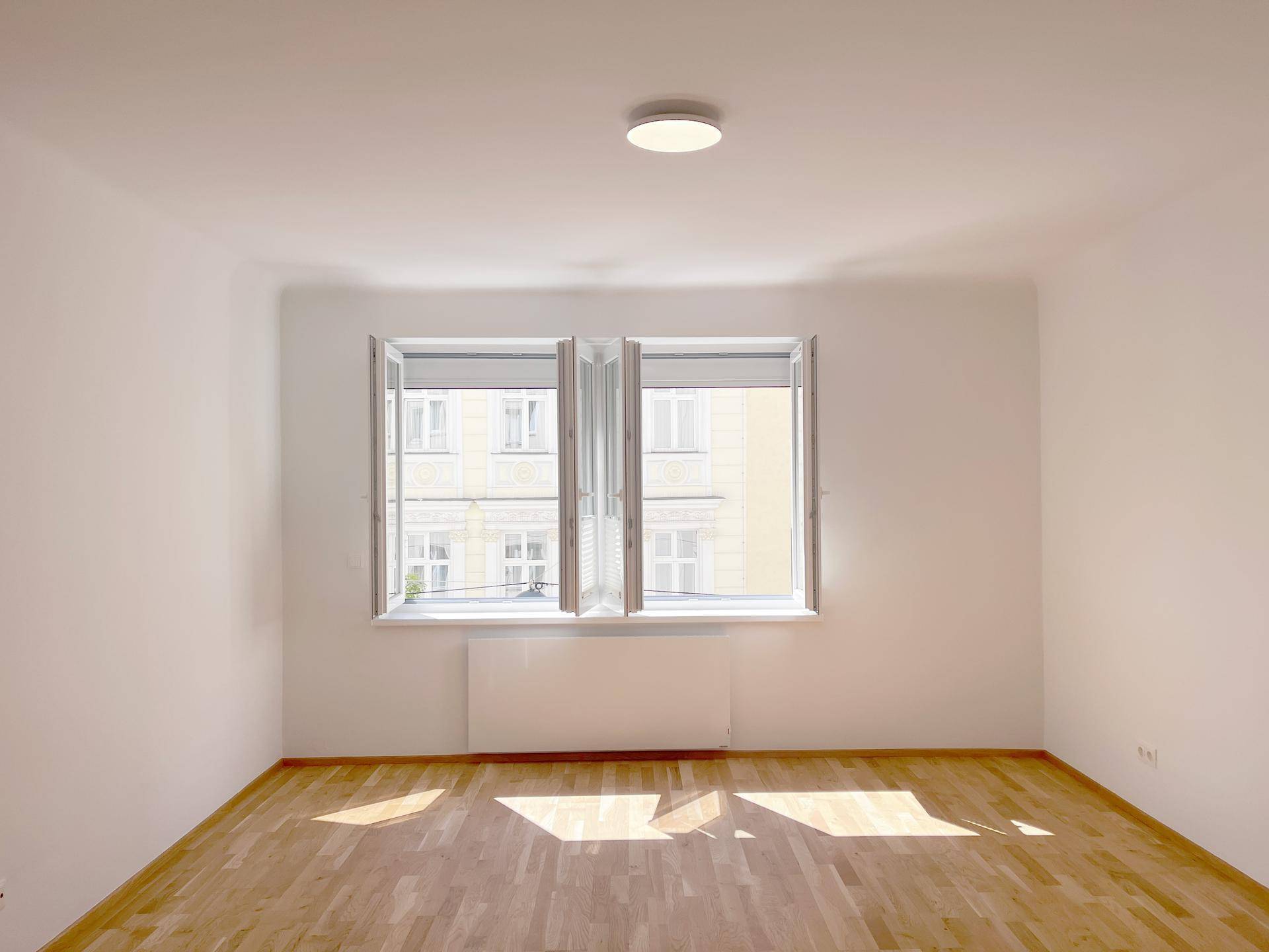 Sonniger Raum mit Parkettboden und geöffneten Fenstern, bietet viel Tageslicht.