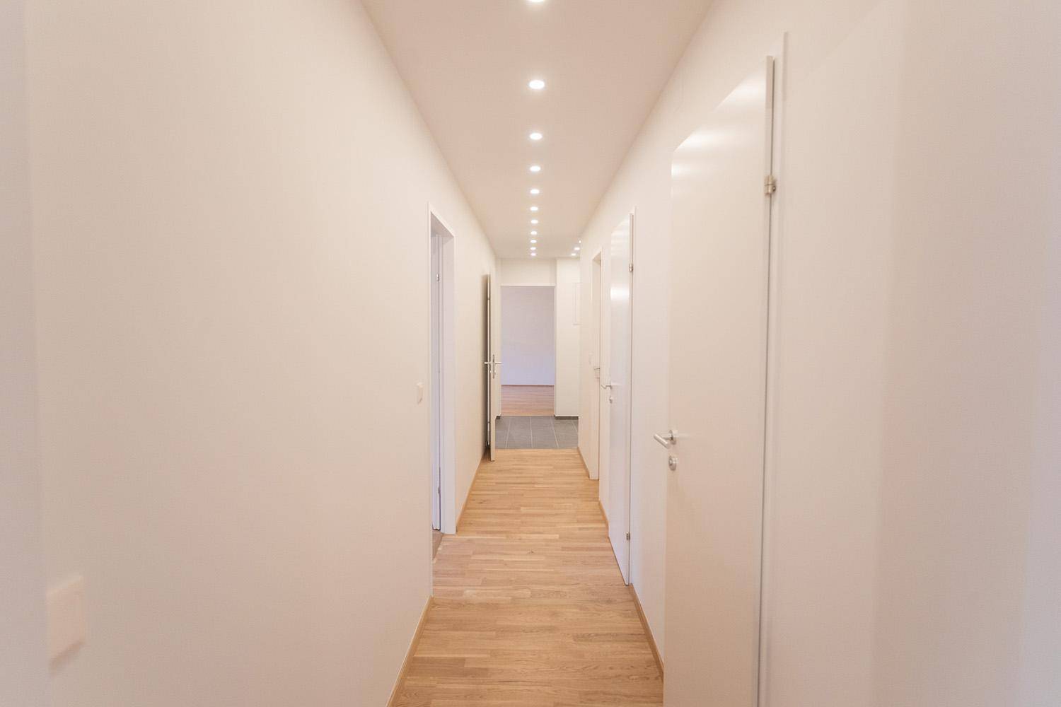 Langer, heller Flur mit durchgehendem Holzfußboden und modernen Einbaustrahlern.