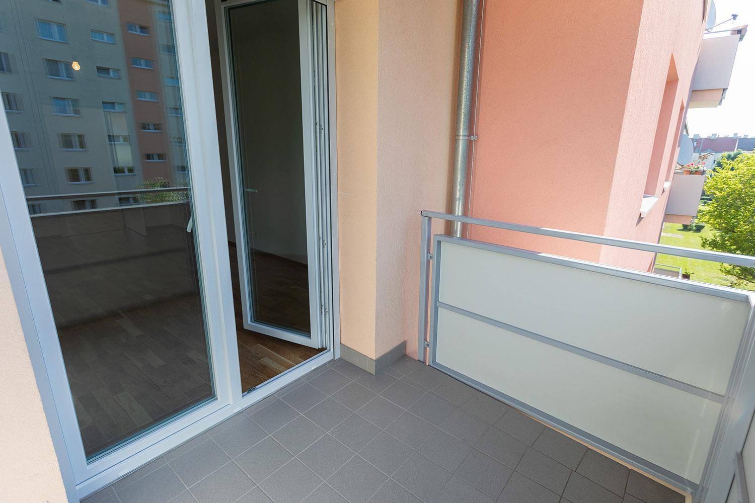 Balkon mit Zugang zum Innenraum, Fliesenboden und Blick auf die Umgebung.