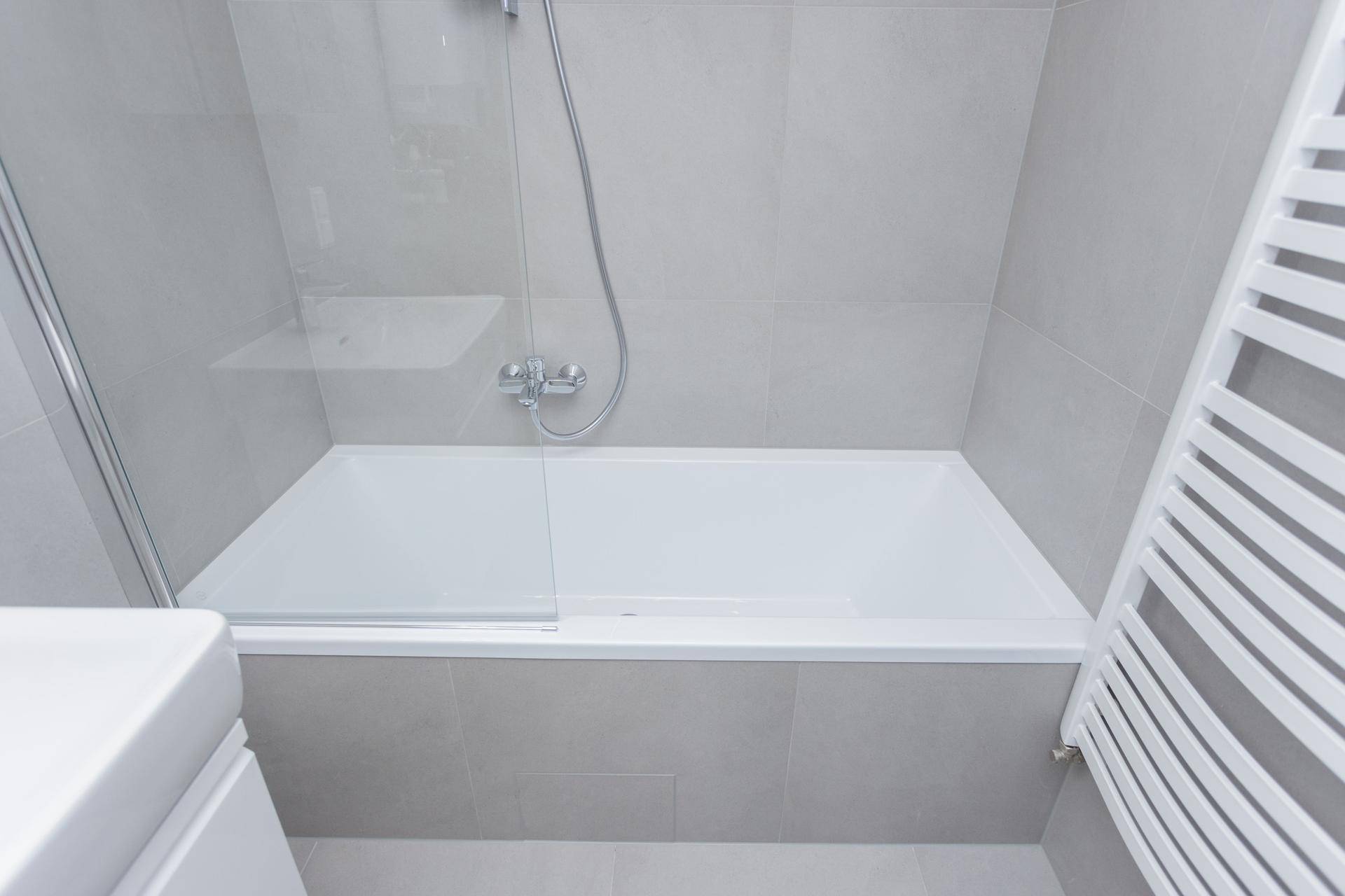 Nahaufnahme der Badewanne mit Glasduschwand und beheiztem Handtuchhalter im modernen Bad.