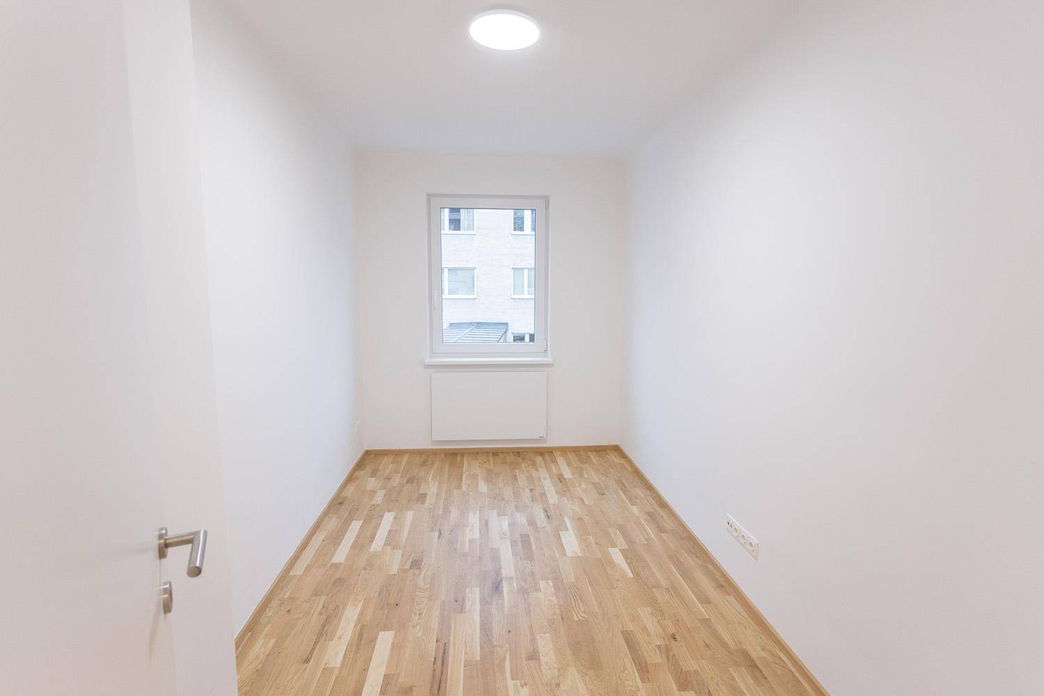 Leeres, helles Zimmer mit Holzboden und einem Fenster, bereit zur individuellen Gestaltung.