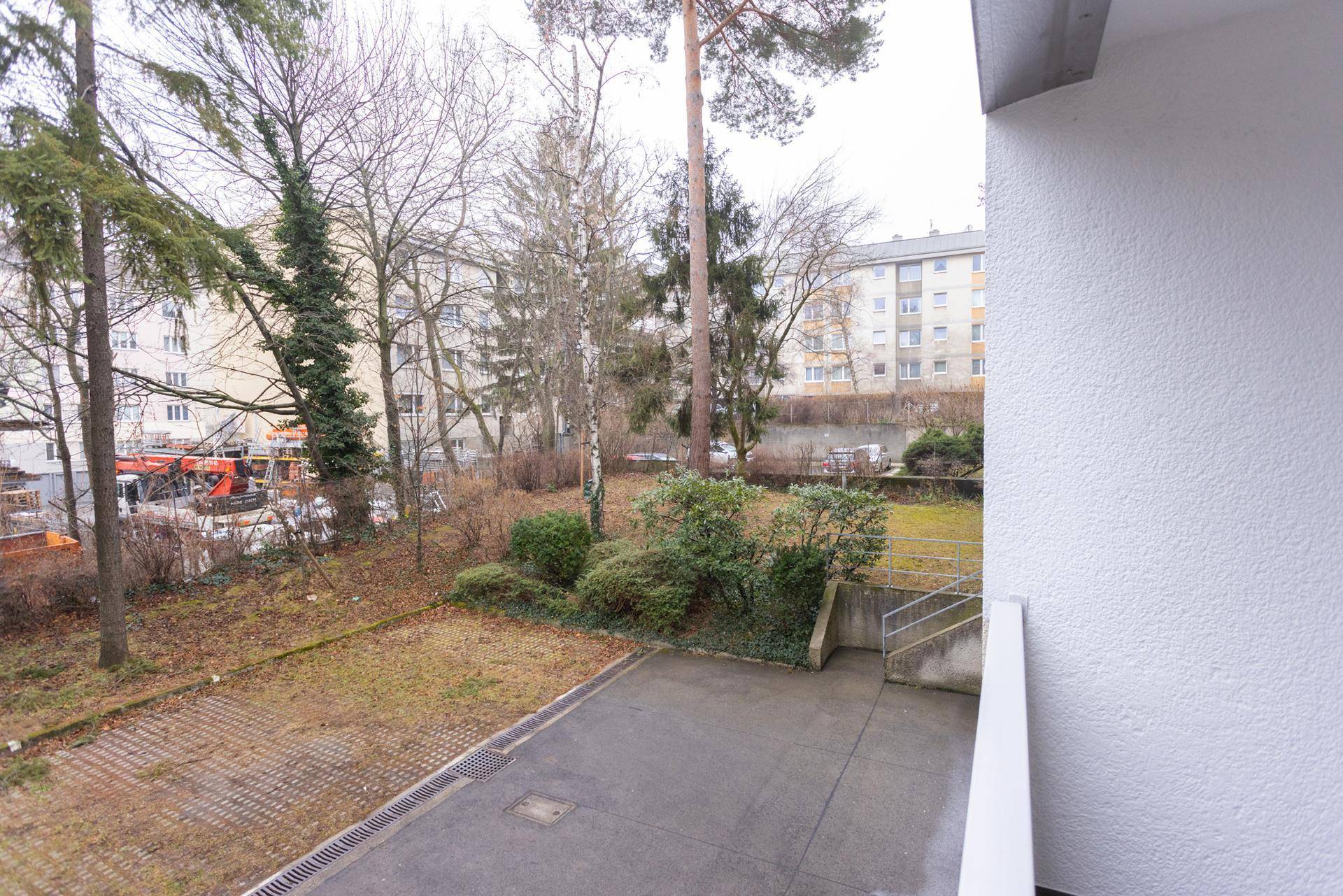 Blick vom Balkon auf einen begrünten Innenhof mit Bäumen und Parkplätzen.
