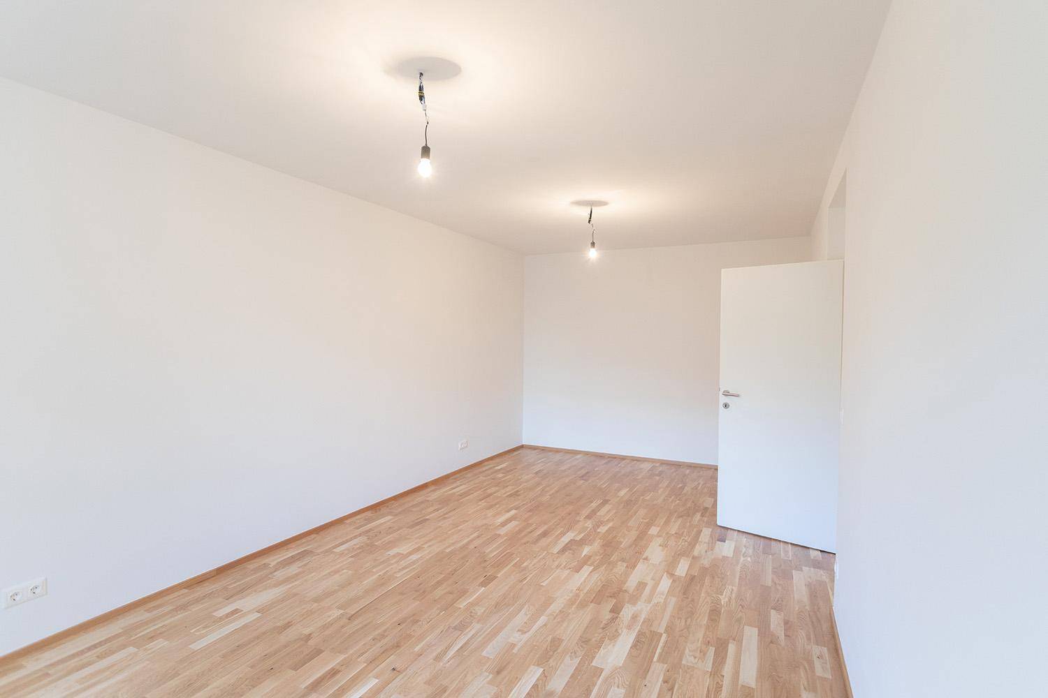 Helles, leeres Zimmer mit Holzboden und weiß gestrichenen Wänden, bereit zur Einrichtung.