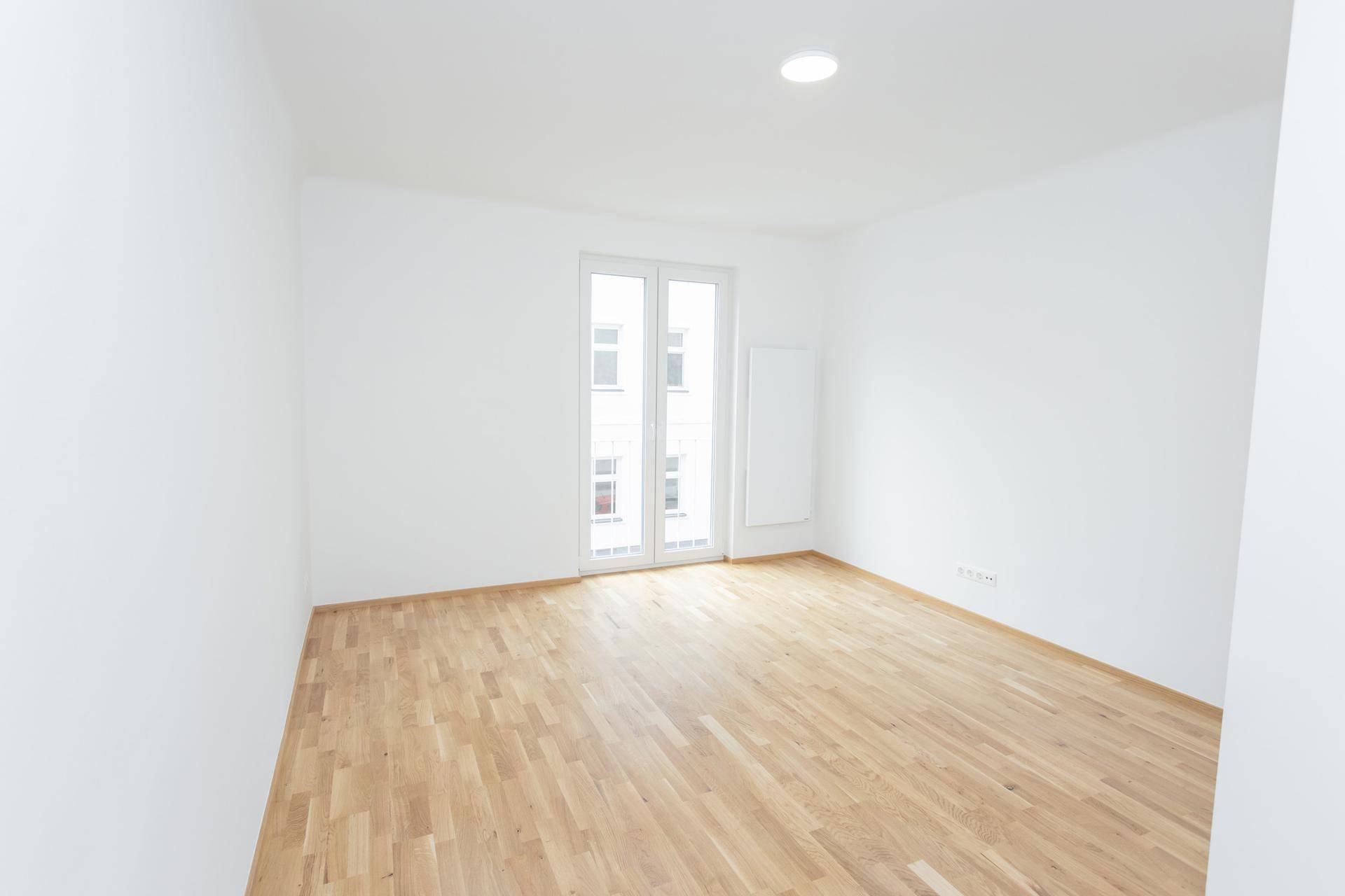 Geräumiger, heller Raum mit Holzboden und französischem Balkon, ideal für Wohnzwecke.