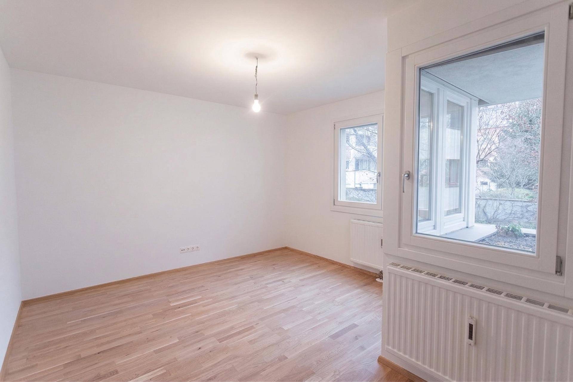 Heller, unmöblierter Raum mit Parkettboden, weißen Wänden und Zugang zu einem kleinen Balkon.