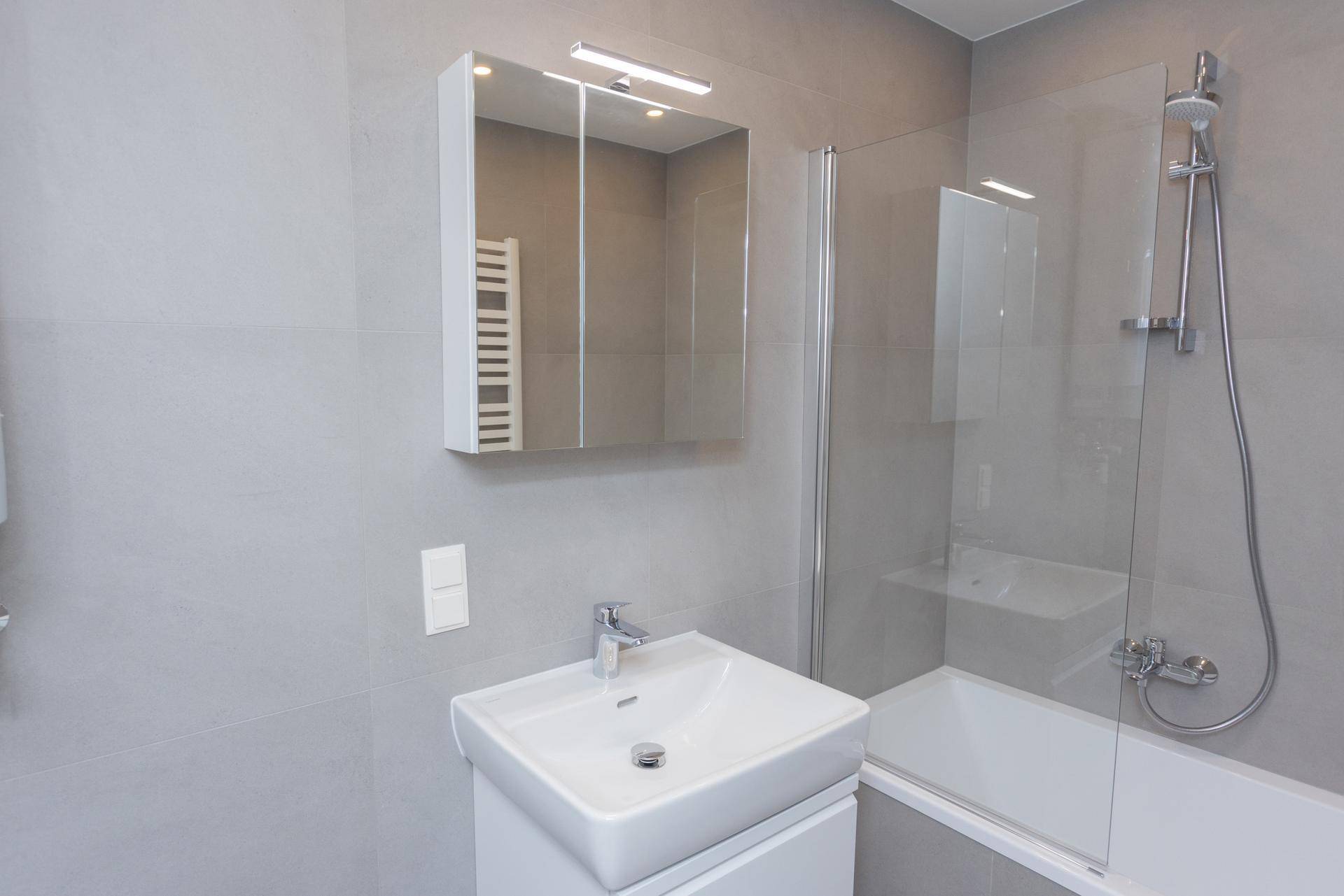 Modernes Badezimmer mit Waschbecken, Spiegelschrank und Badewanne mit Glasduschwand.