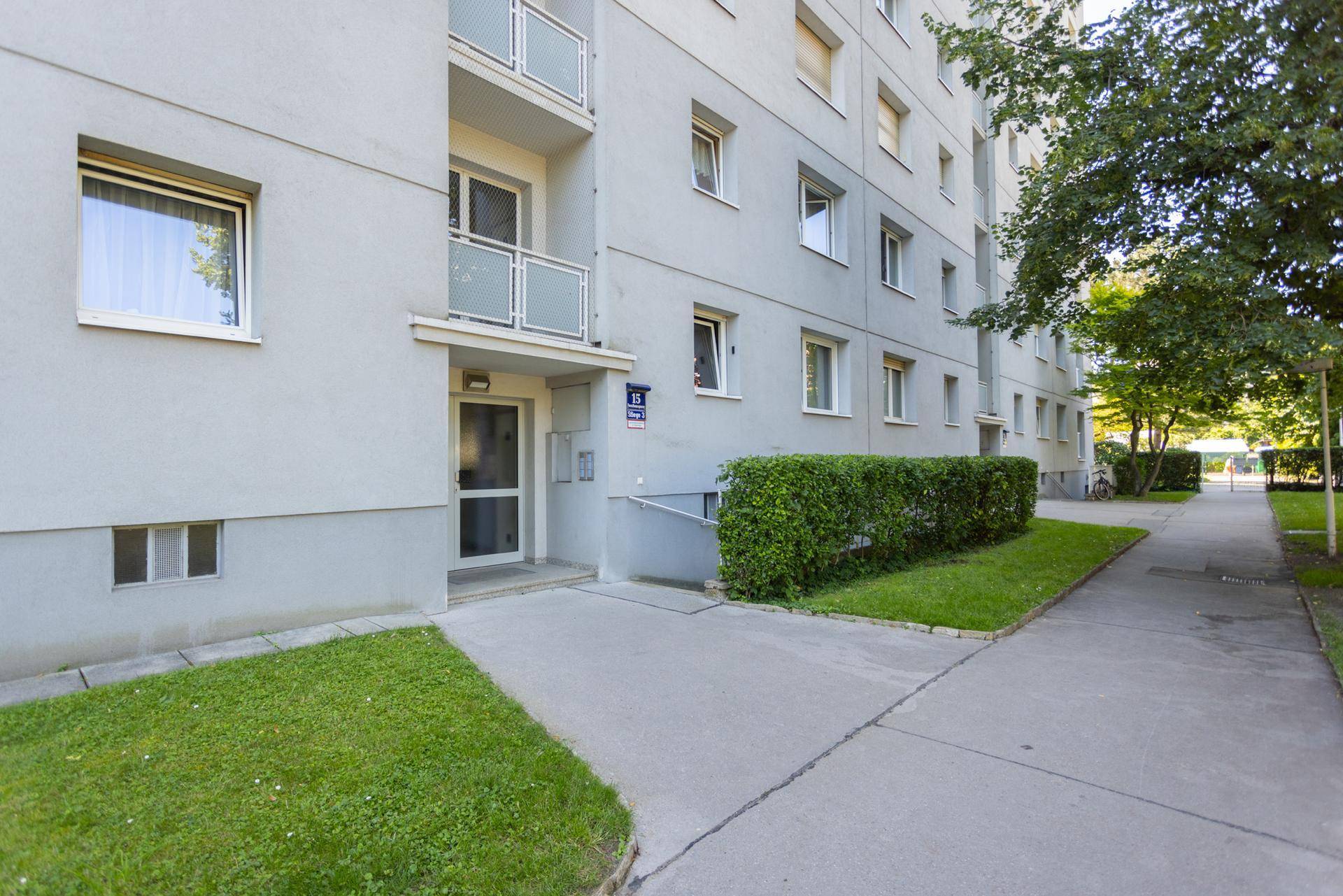 Eingangsbereich eines Mehrfamilienhauses mit Rampe für Barrierefreiheit und gepflegter Hecke.
