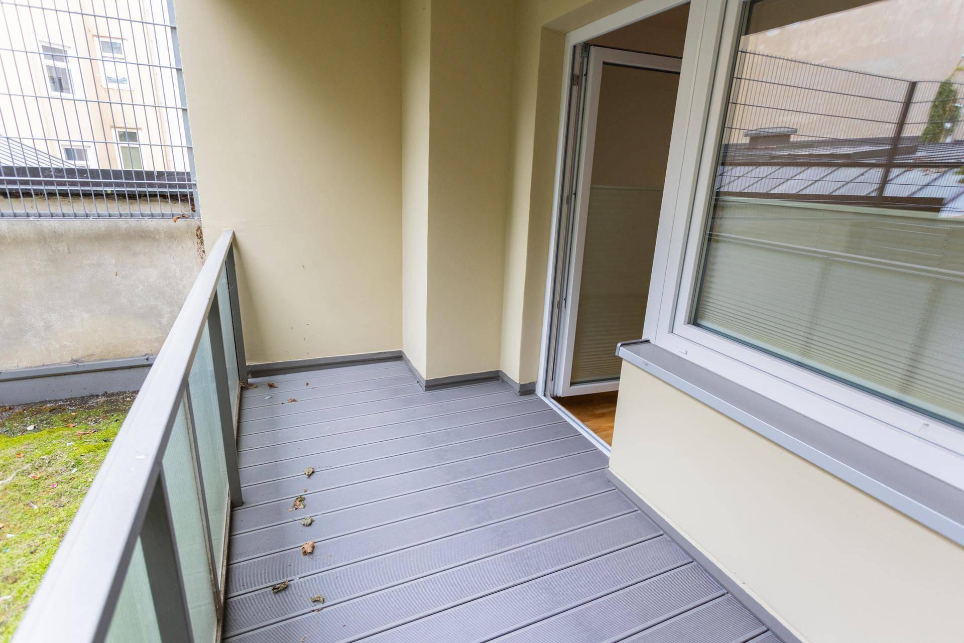 Kleiner Balkon mit grauem Dielenboden und Blick auf eine Rasenfläche und einen Zaun.