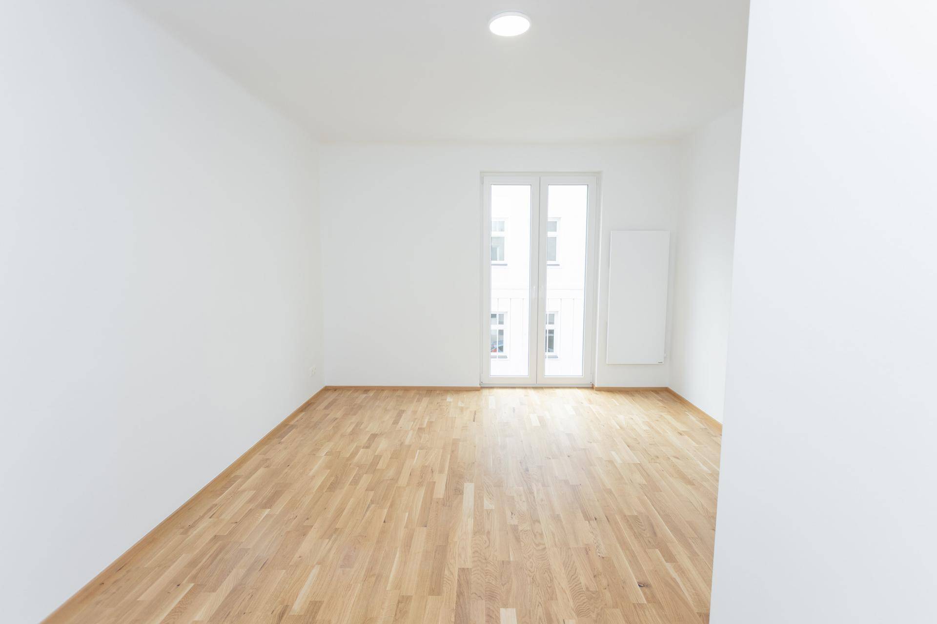 Heller, unmöblierter Raum mit Holzboden und Zugang zu einem französischen Balkon.
