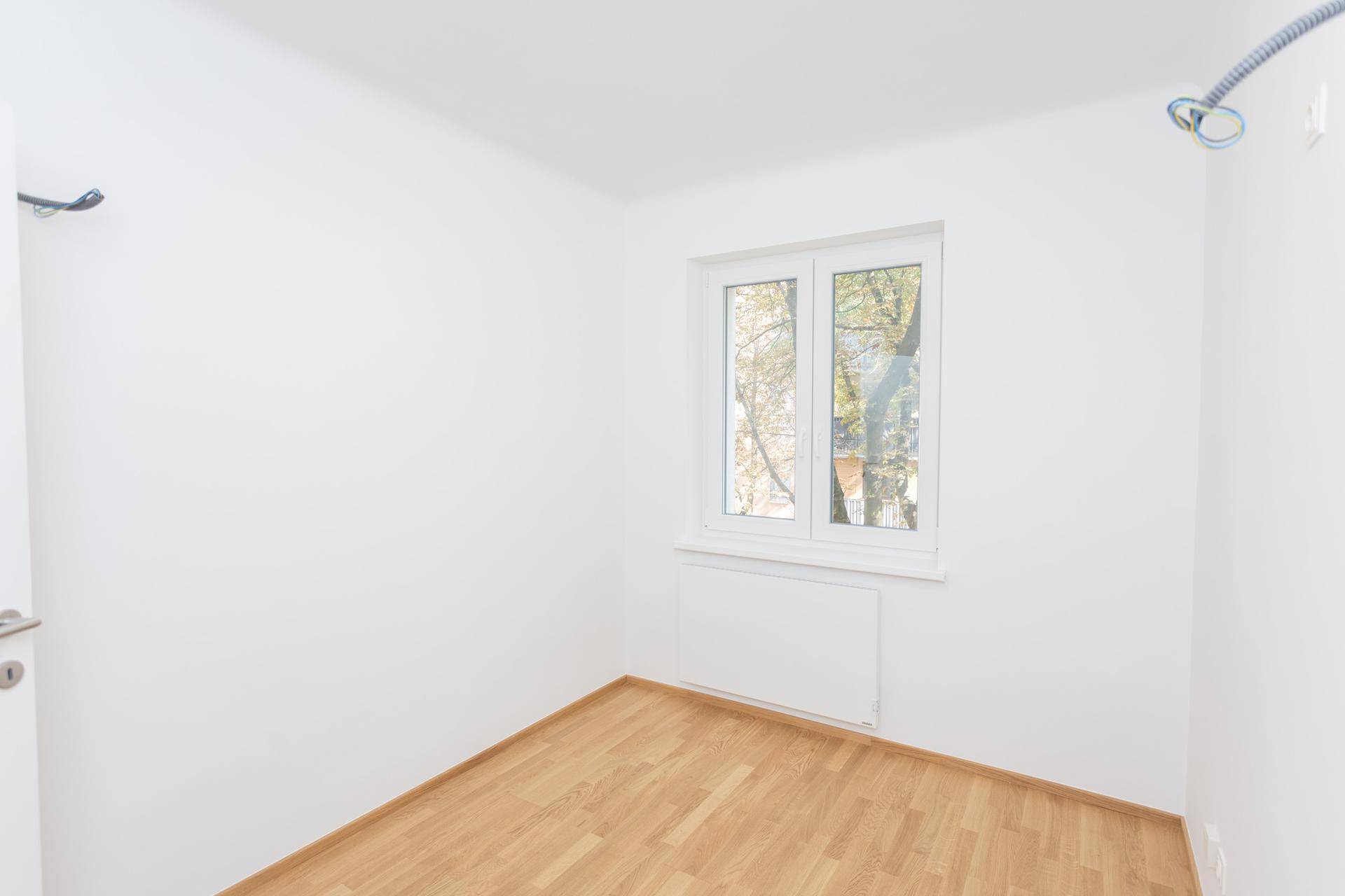 Helles, leeres Zimmer mit Holzparkettboden und einem Fenster, das viel Licht spendet.