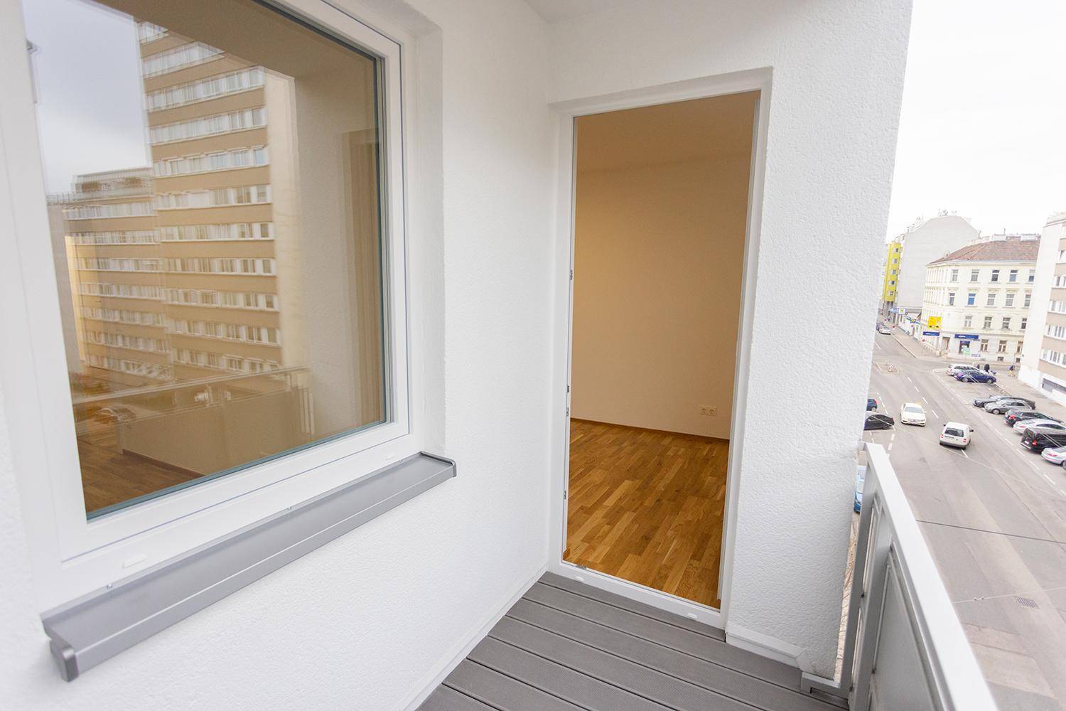 Balkon mit grauem Bodenbelag und Zugang zu einem hellen Innenraum, bietet Stadtblick.